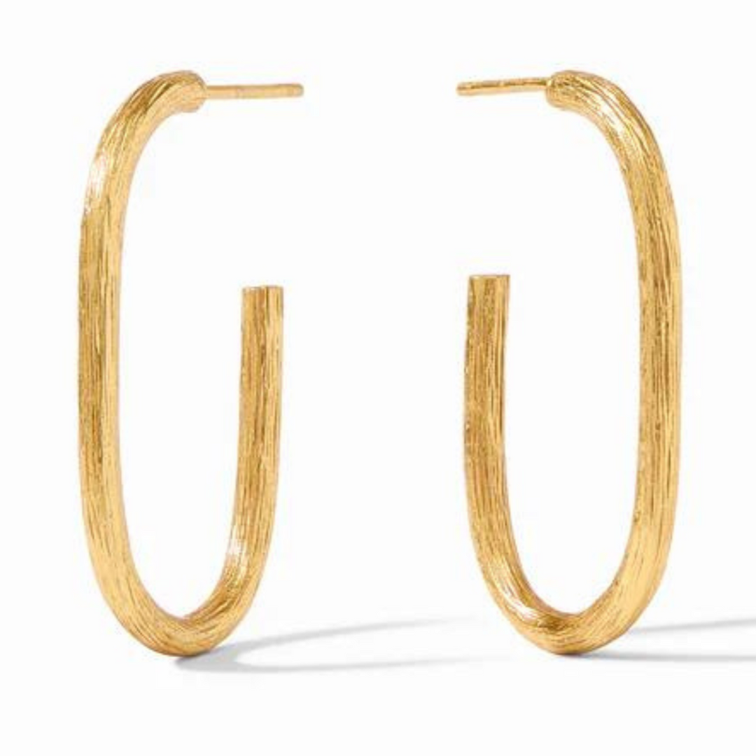 Gold oval hoop earrings pictured on a gold mirror. 