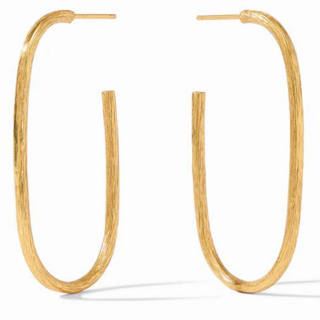 Gold oval hoop earrings pictured on a gold mirror. 
