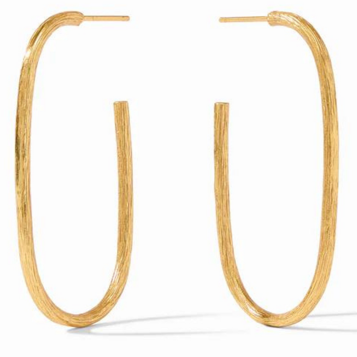 Gold oval hoop earrings pictured on a gold mirror. 