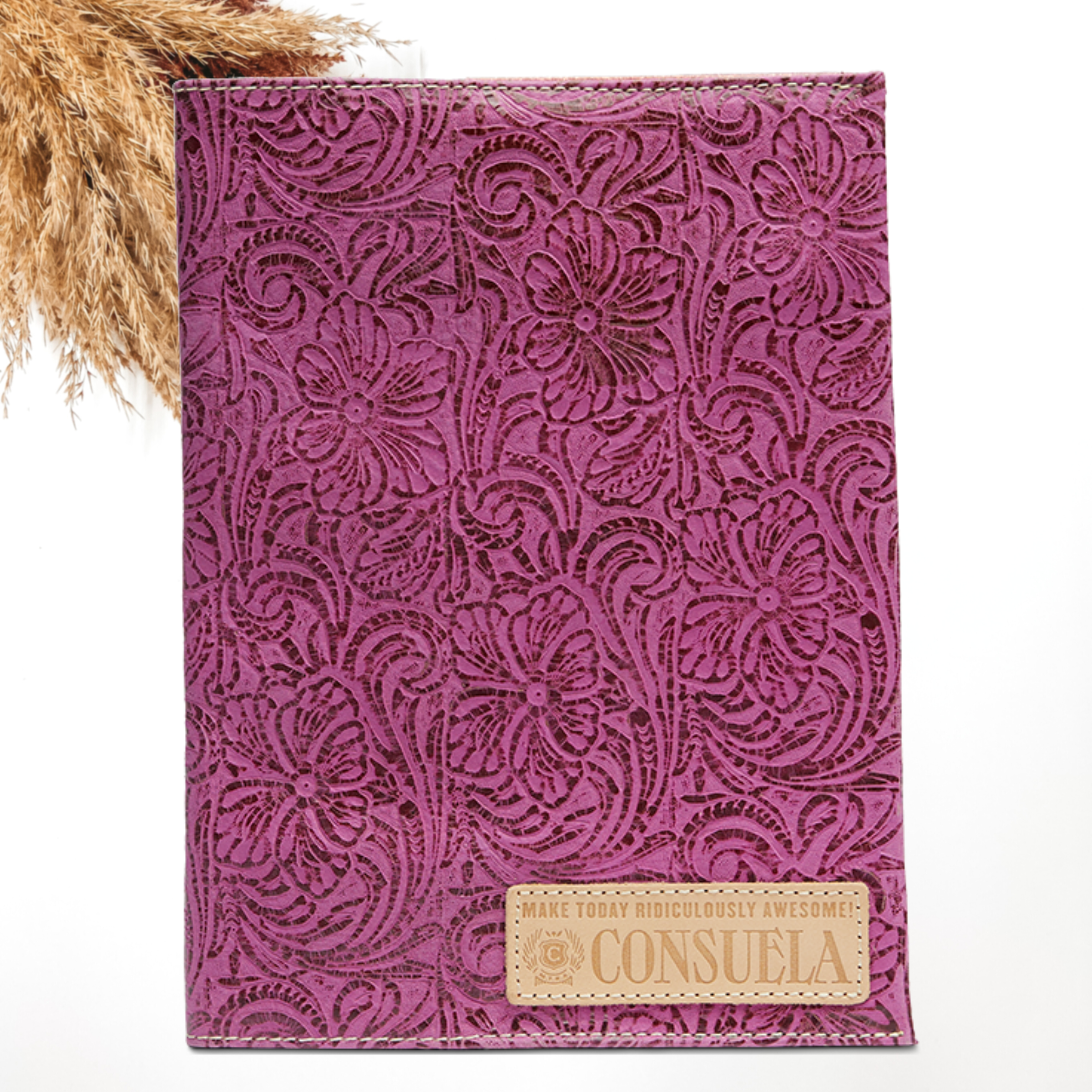 Pictured on a white background is a fuchsia, tooled leather print notebook cover. This notebook includes a light tan leather patch on the bottom right corner.   