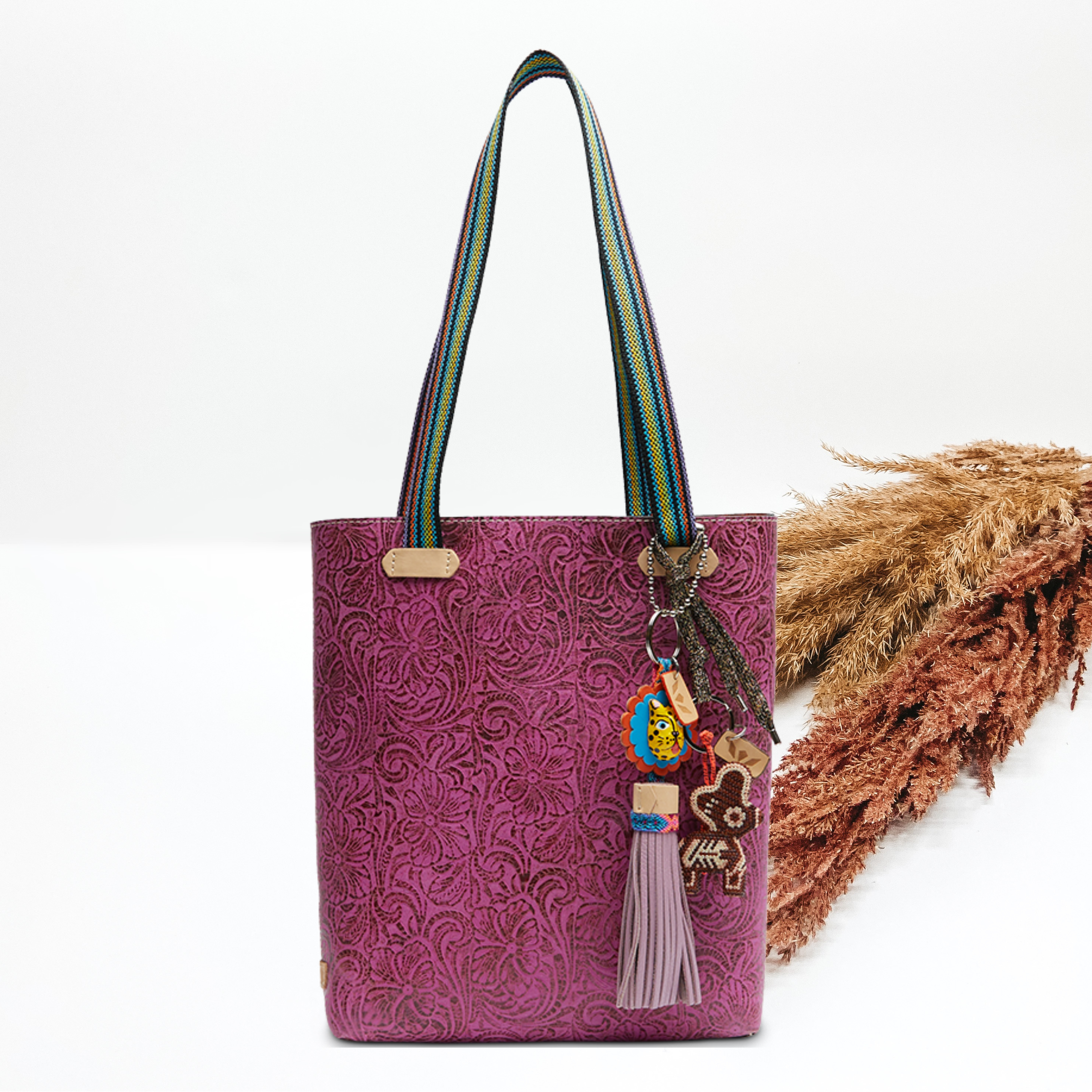Pictured on a white background is a fuchsia, tooled leather print everyday tote. This bad includes striped handles and two multicolored charms.   