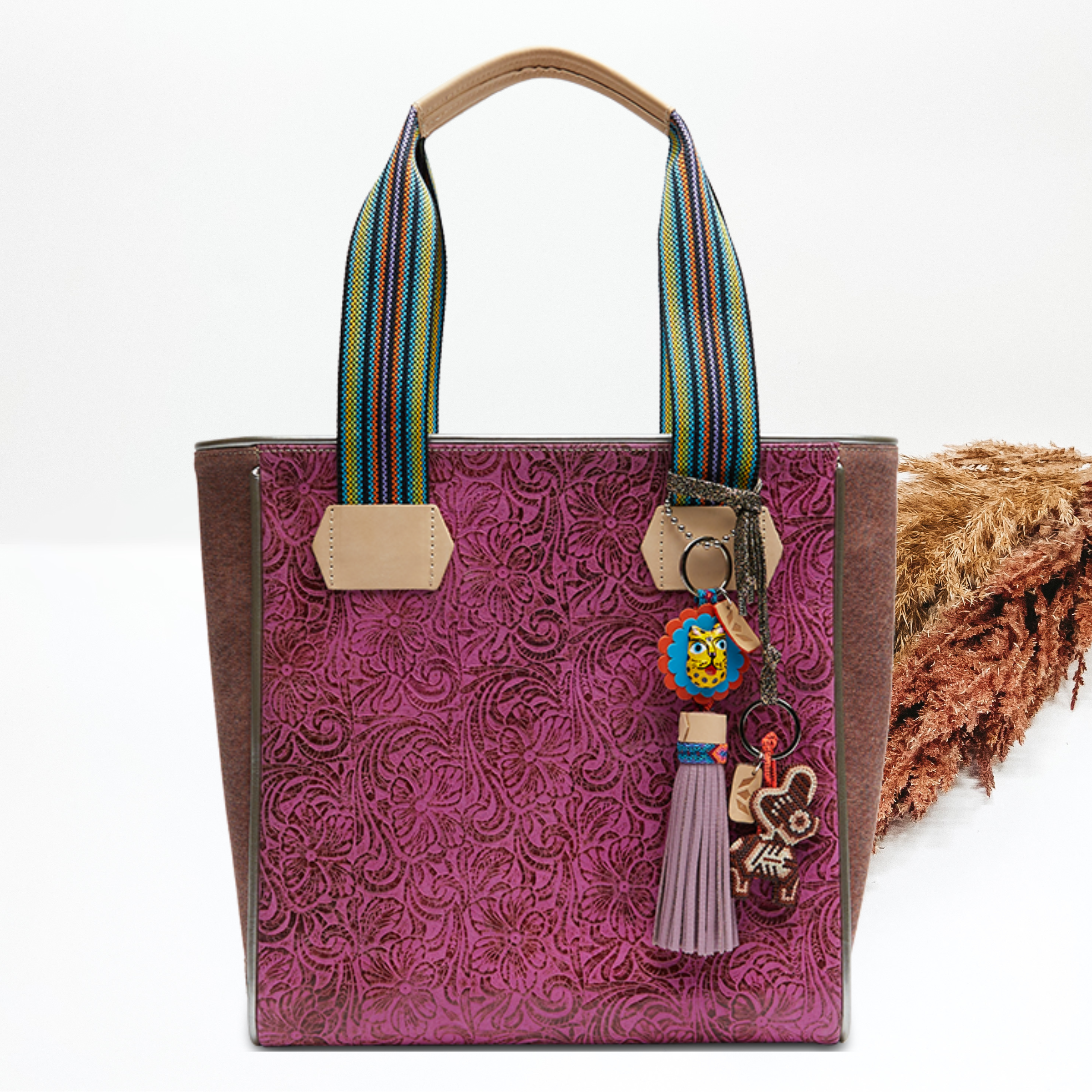 Pictured on a white background is a fuchsia, tooled leather classic tote. This tote includes striped handles and two multicolored charms.   