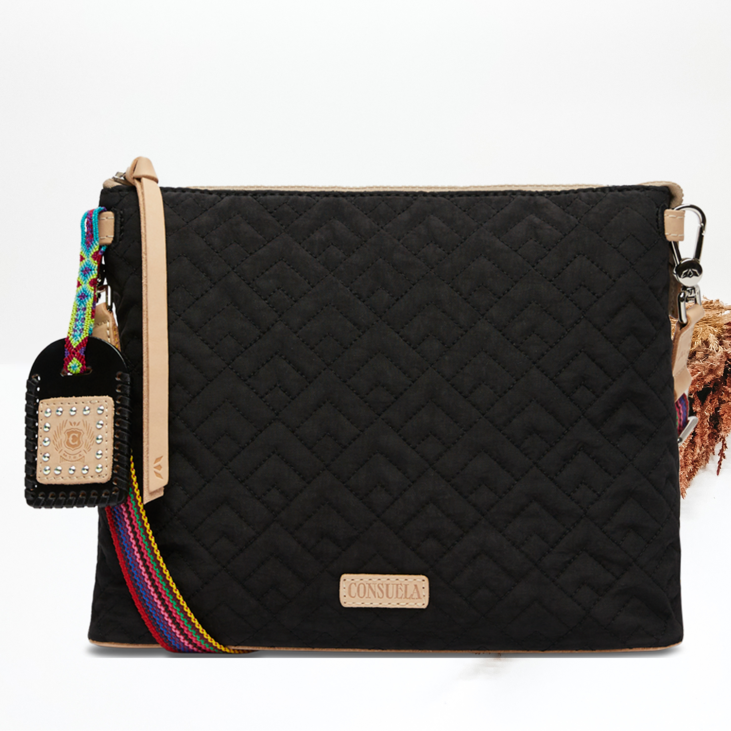 Pictured on a white background is a black downtonw crossbody that has a diamond stitched print. This purse includes a black and tan charm with a striped purse strap. 