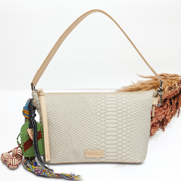 Pictured on a white background is a white snake print your way bag. This purse includes multiple, multicolored charms and a light tan shoulder strap. 