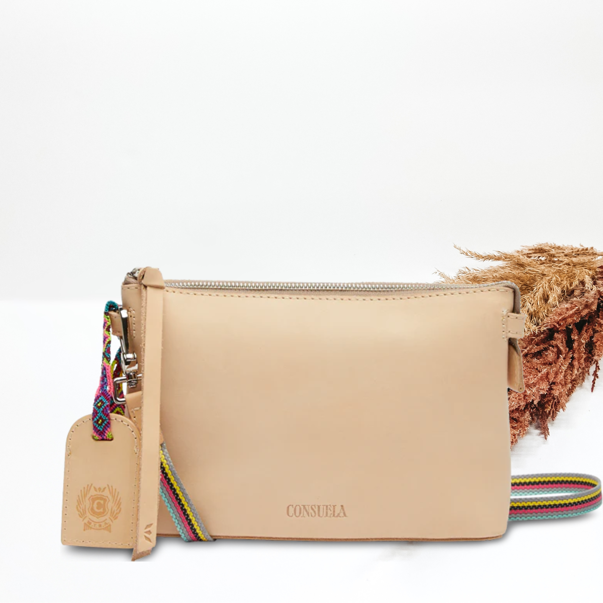 A light brown leather purse with a crossbody strap. Pictured on white background with brown pompous grass on the right side. 