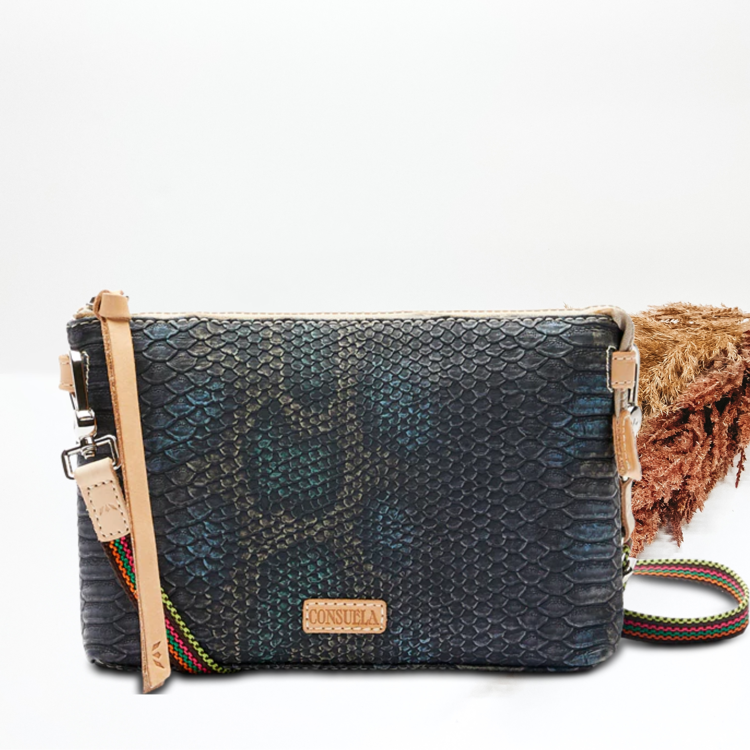 A blue and black snake print purse with a crossbody strap. Pictured on white background with brown pompous grass on the right side. 