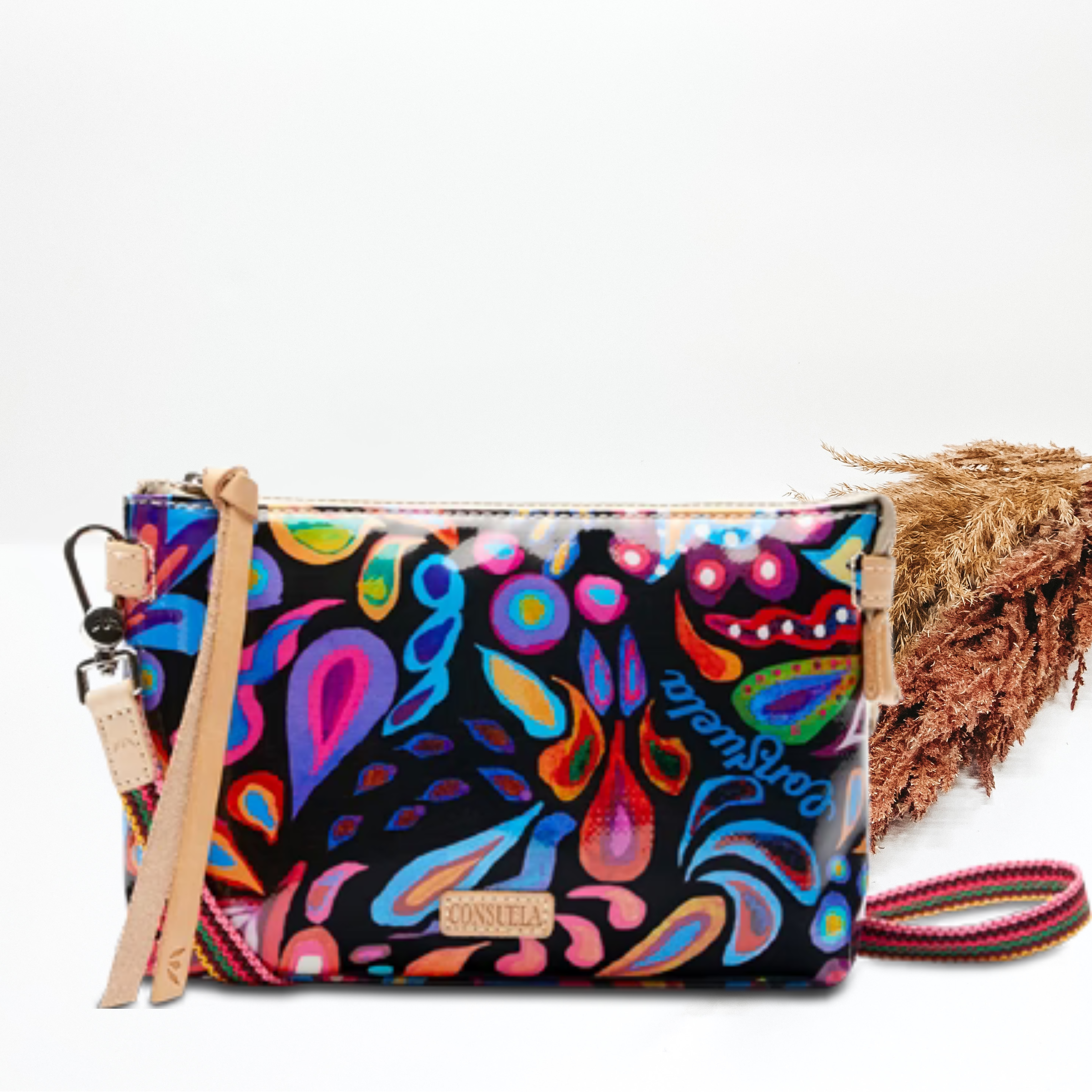 A multicolor sophie print purse with a crossbody strap. Pictured on white background with brown pompous grass on the right side. 