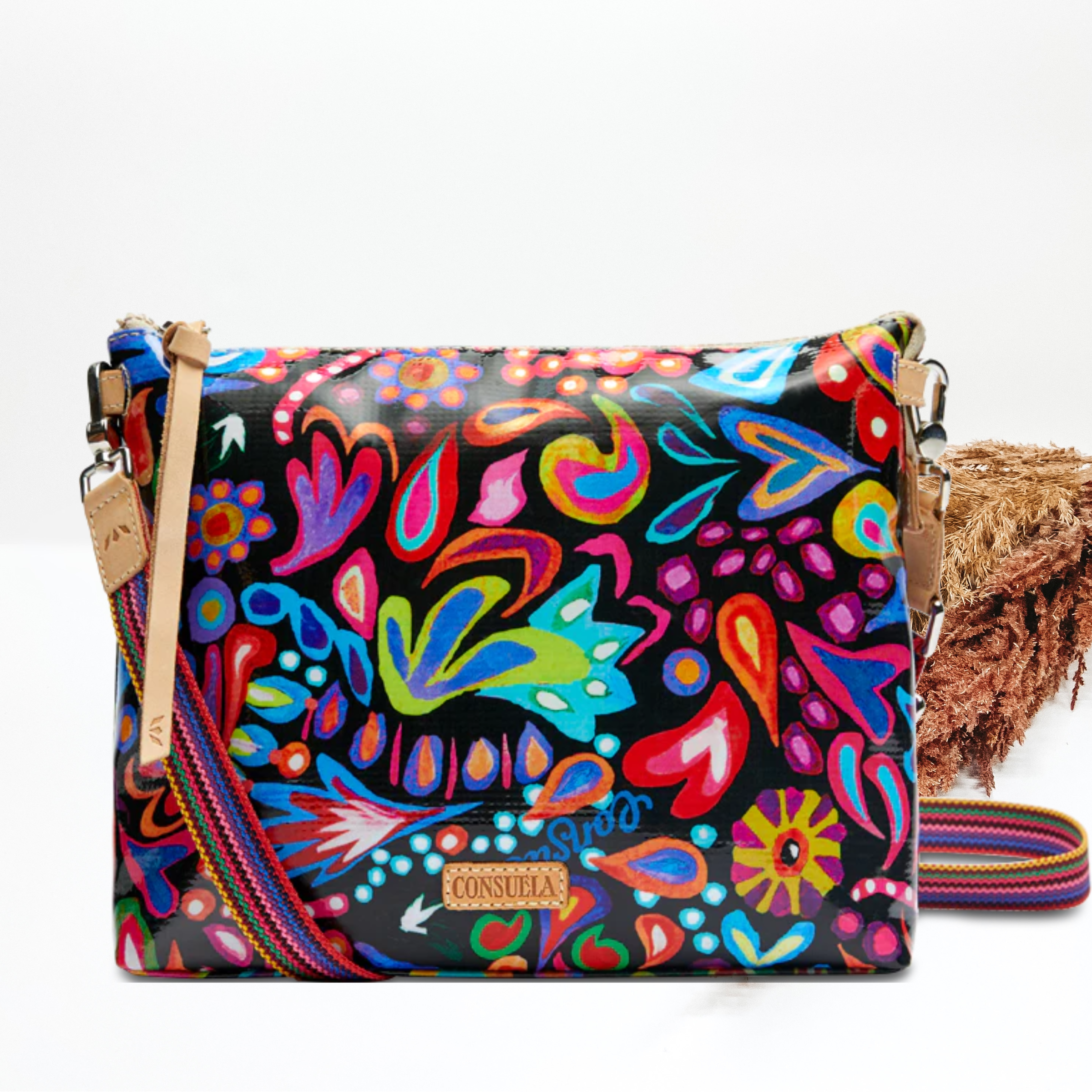 A black crossbody bag with multicolor floral and paisley print. Pictured on white background with brown pompous grass on the right side.