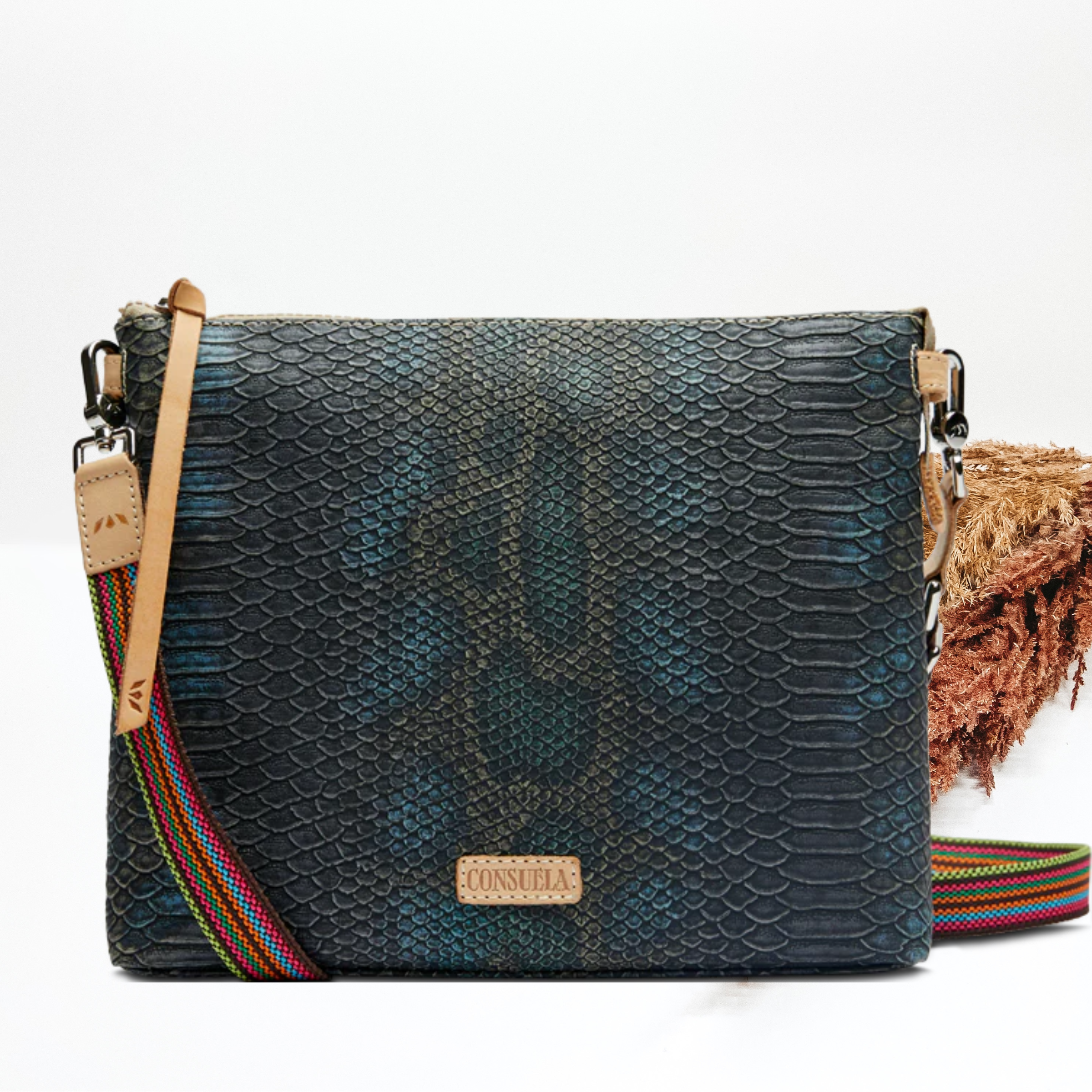 A black and blue snake print purse with a crossbody strap. Pictured on white background with brown pompous grass on the right side. 