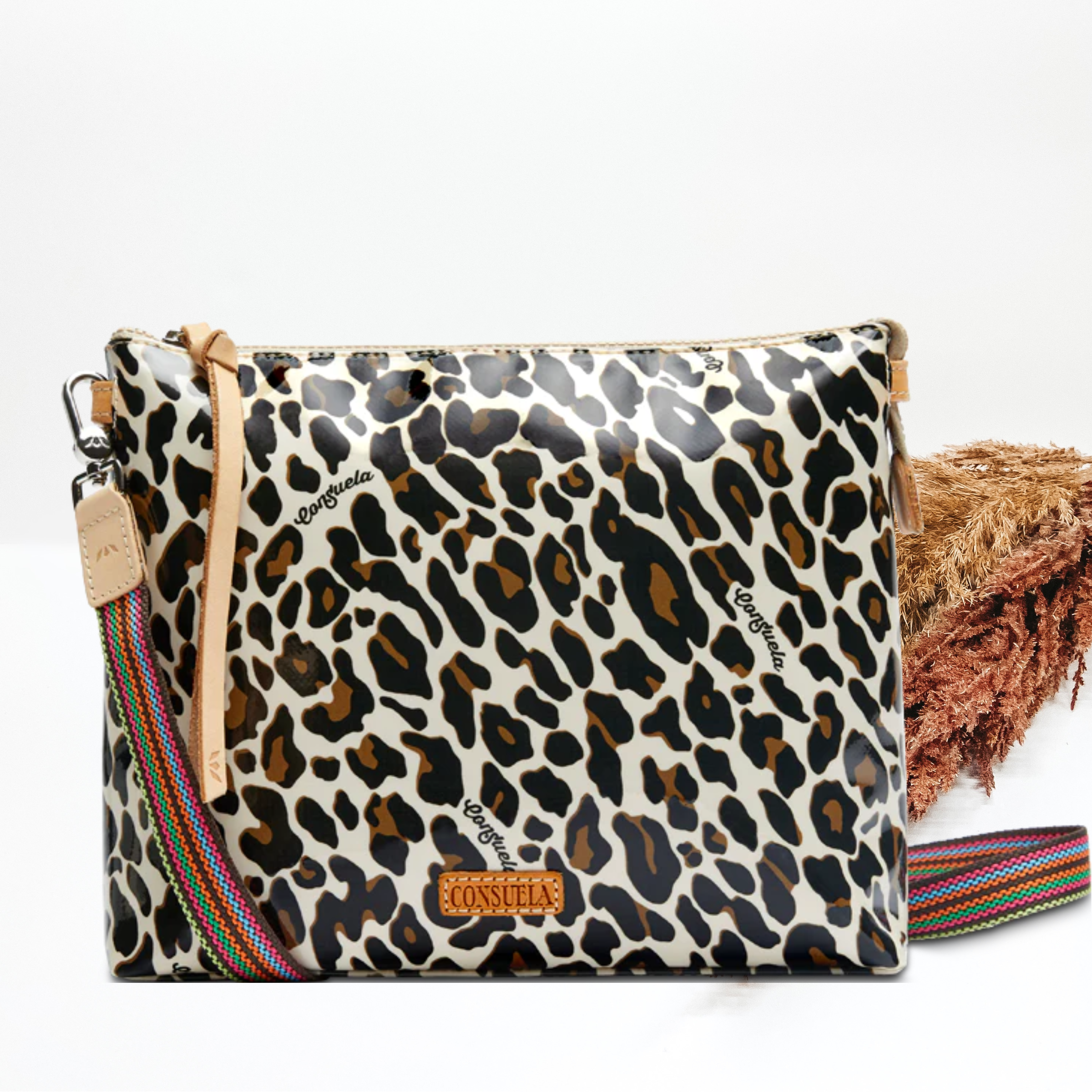 A leopard print crossbody bag with a colorful strap. Pictured on white background with brown pompous grass on the right side.