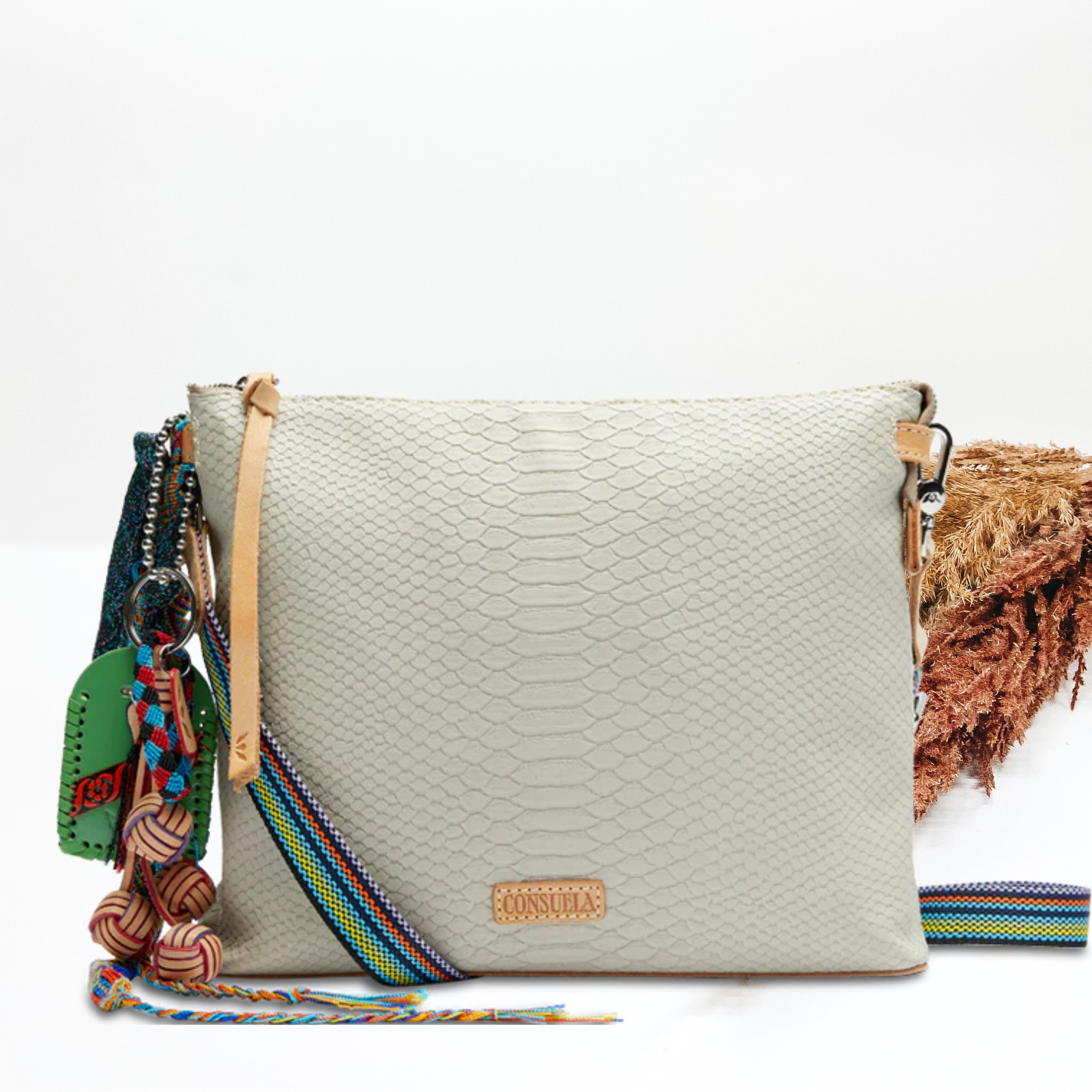 An ivory snake print crossbody purse. Pictured on white background with brown pompous grass on the right side.