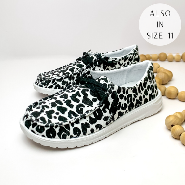 Pictured are a pair of black and white leopard print canvas shoes with a white sole and black laces. These shoes are pictured on a white background with tan beads on the right side.