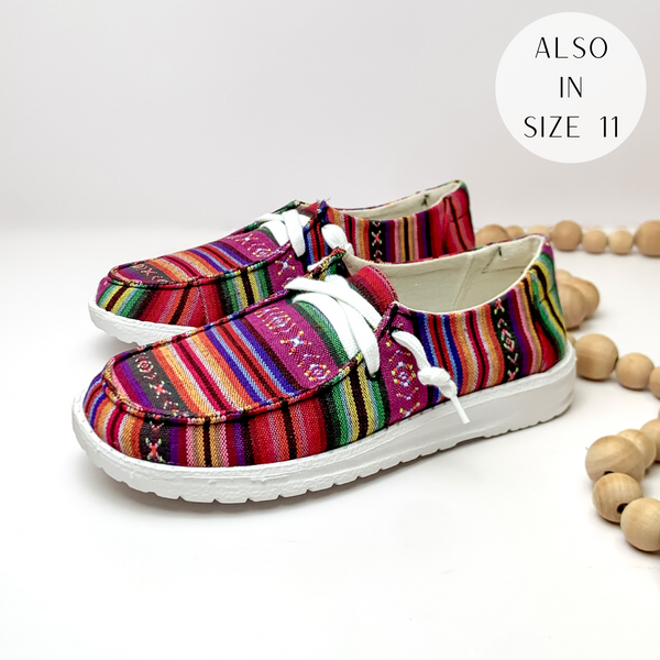 Pictured are a pair of multicolored serape print canvas shoes with a white sole and white laces. These shoes are pictured on a white background with tan beads on the right side.