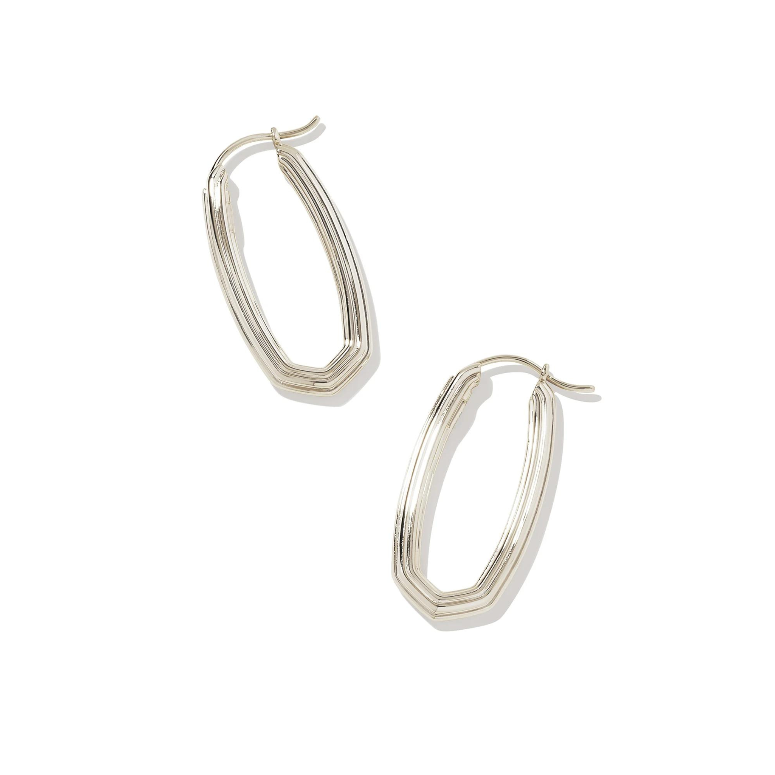 Pictured is a pair of silver, oval, ridged texture hoops on a white background. 