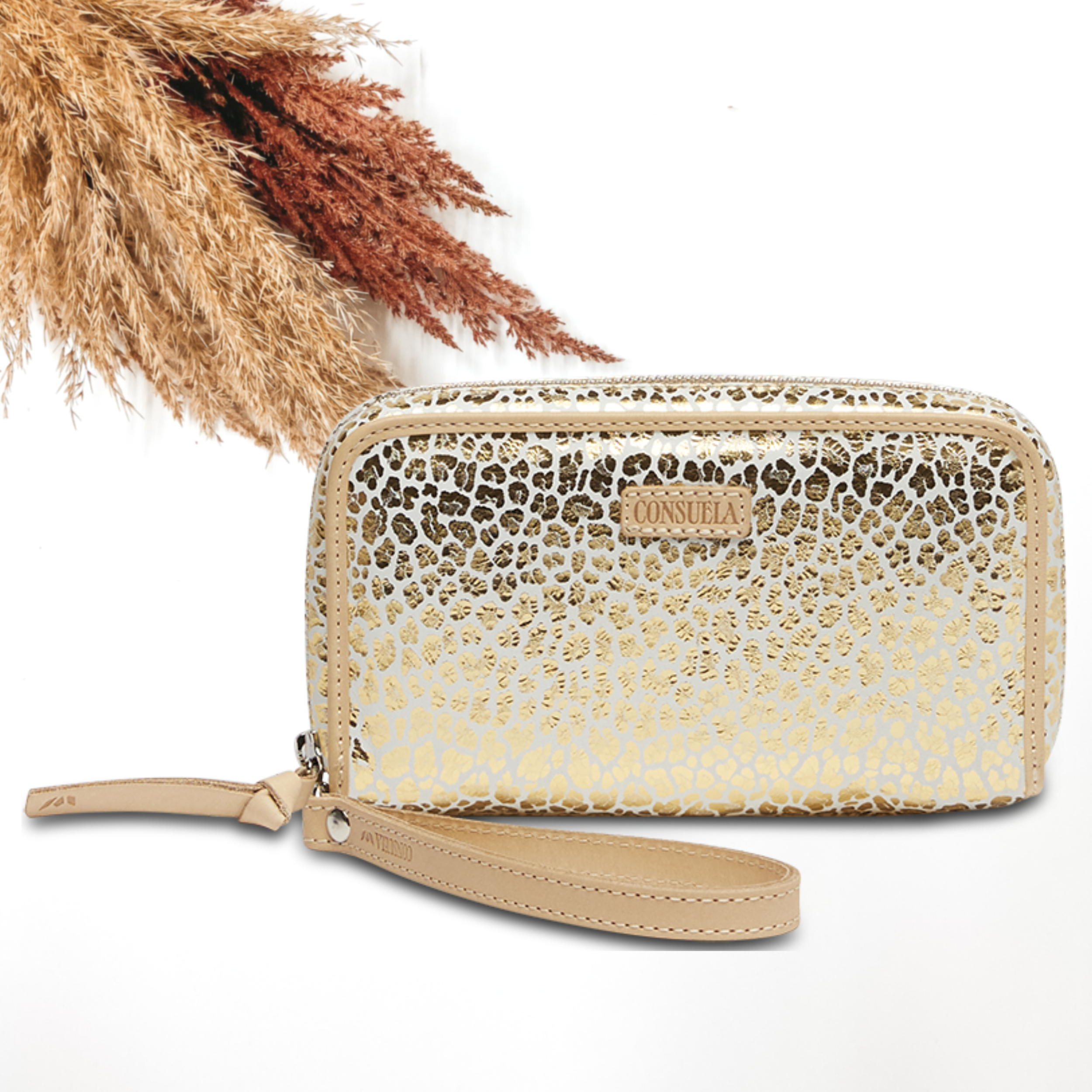 Pictured on a white background is a wristlet wallet with a light tan leather wristlet strap. This wallet has a white with a metallic gold leopard print design. 