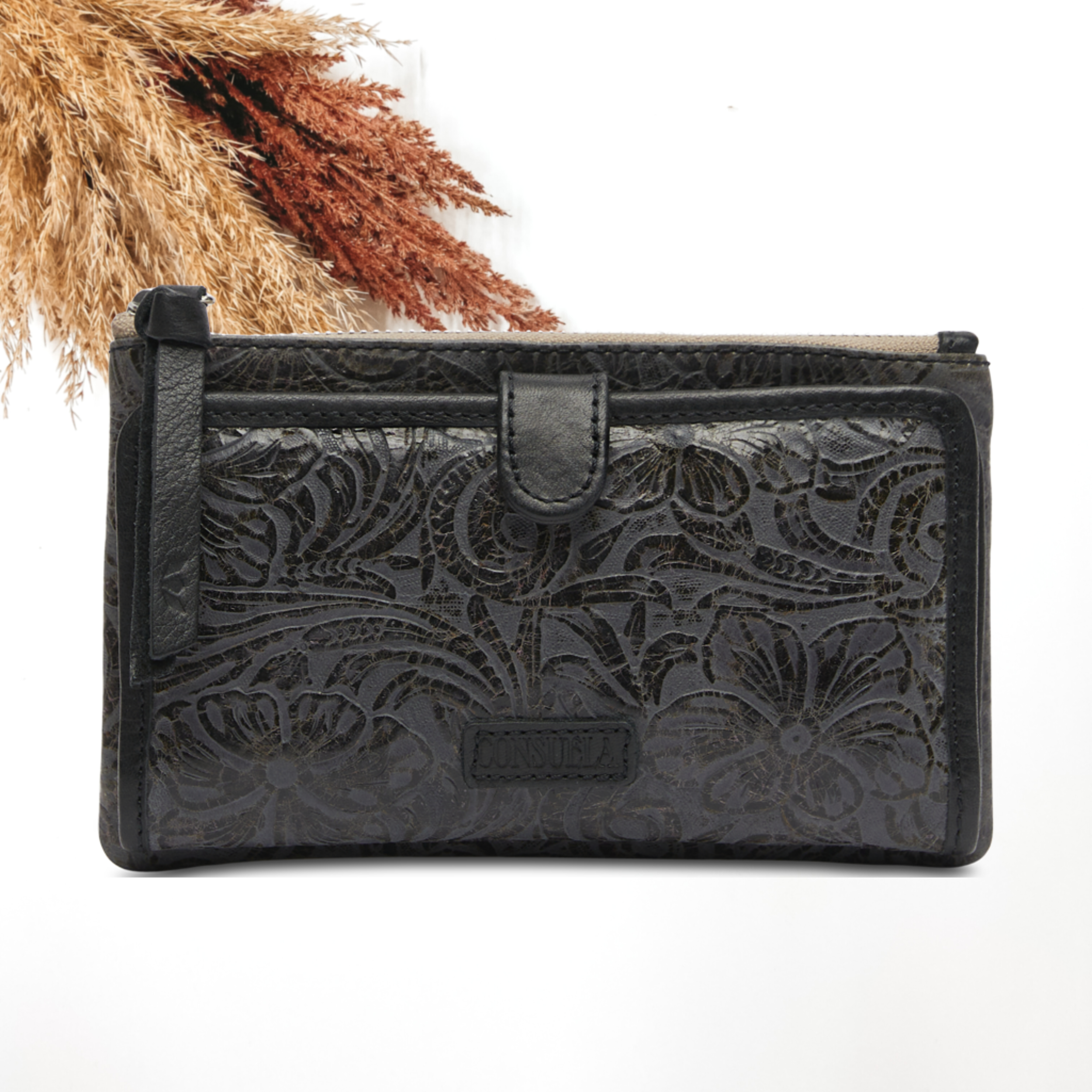 Pictured on a white background is a slim wallet with a black tassel zipper pull. This wallet has a black leather tooled design. 