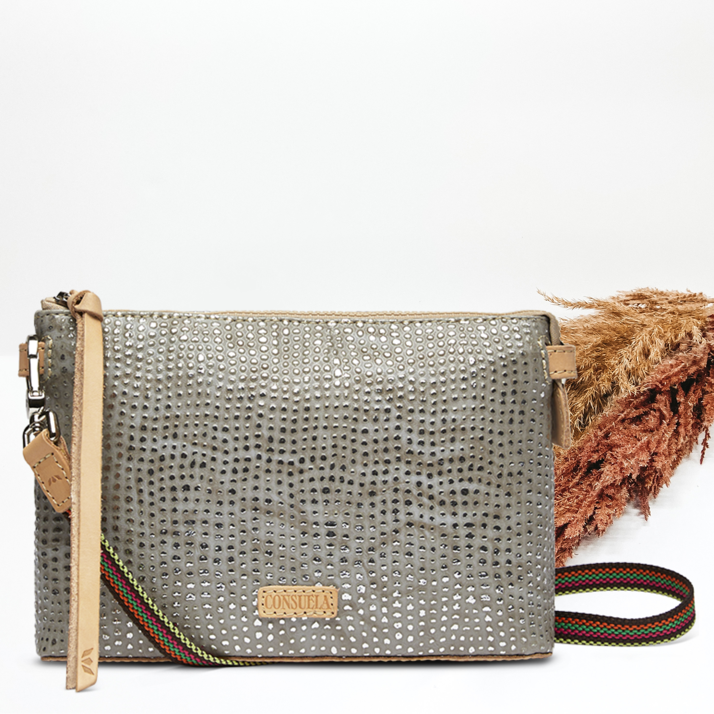 Pictured on a white background is a grey midtown corssbody purse with silver dotted print. This purse has a woven crossbody strap and light tan leather zipper pull.