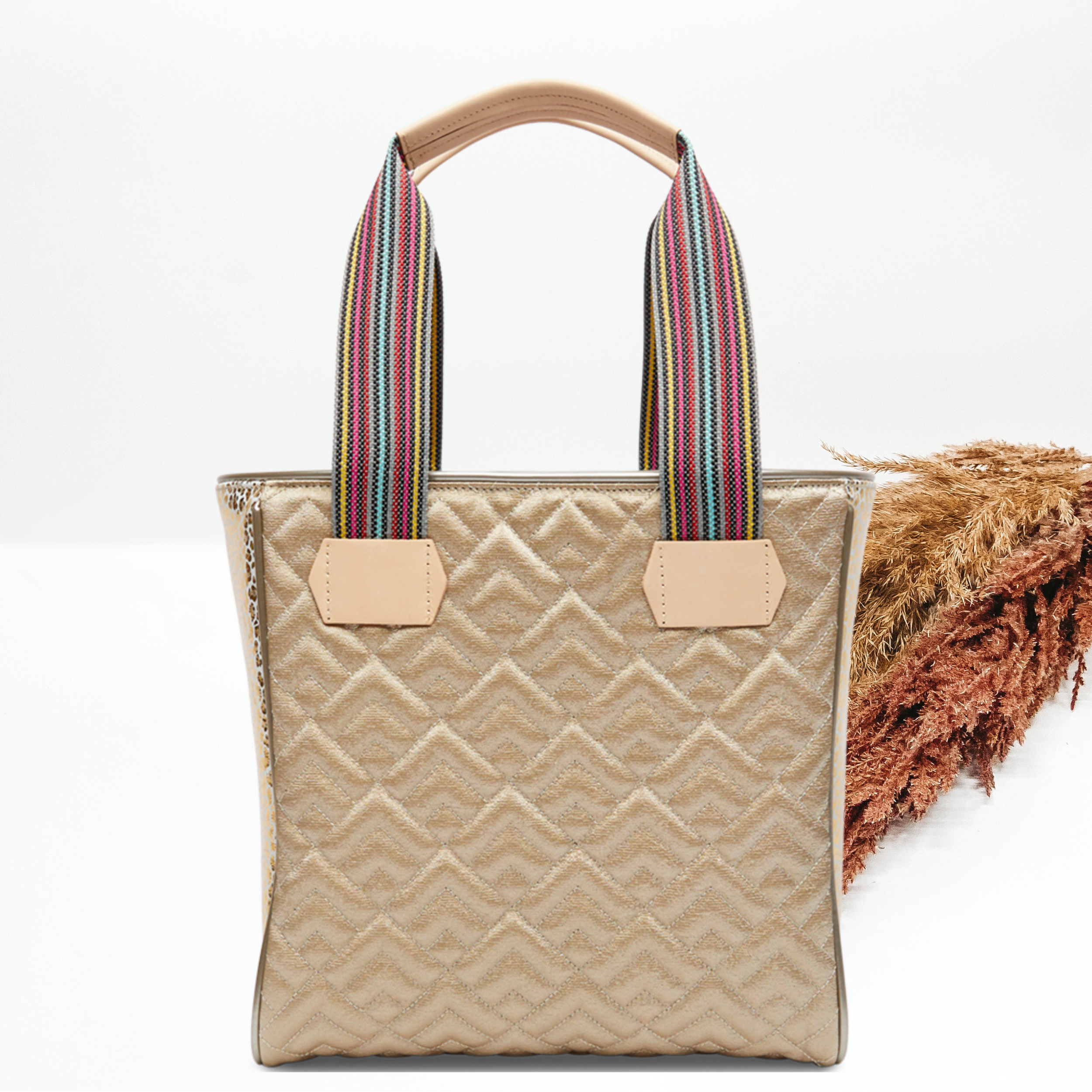 Pictured on a white background is a gold classic tote bag with woven straps and light tan handles. This bag includes a diamond stitched pattern and gold leopard side panels. 