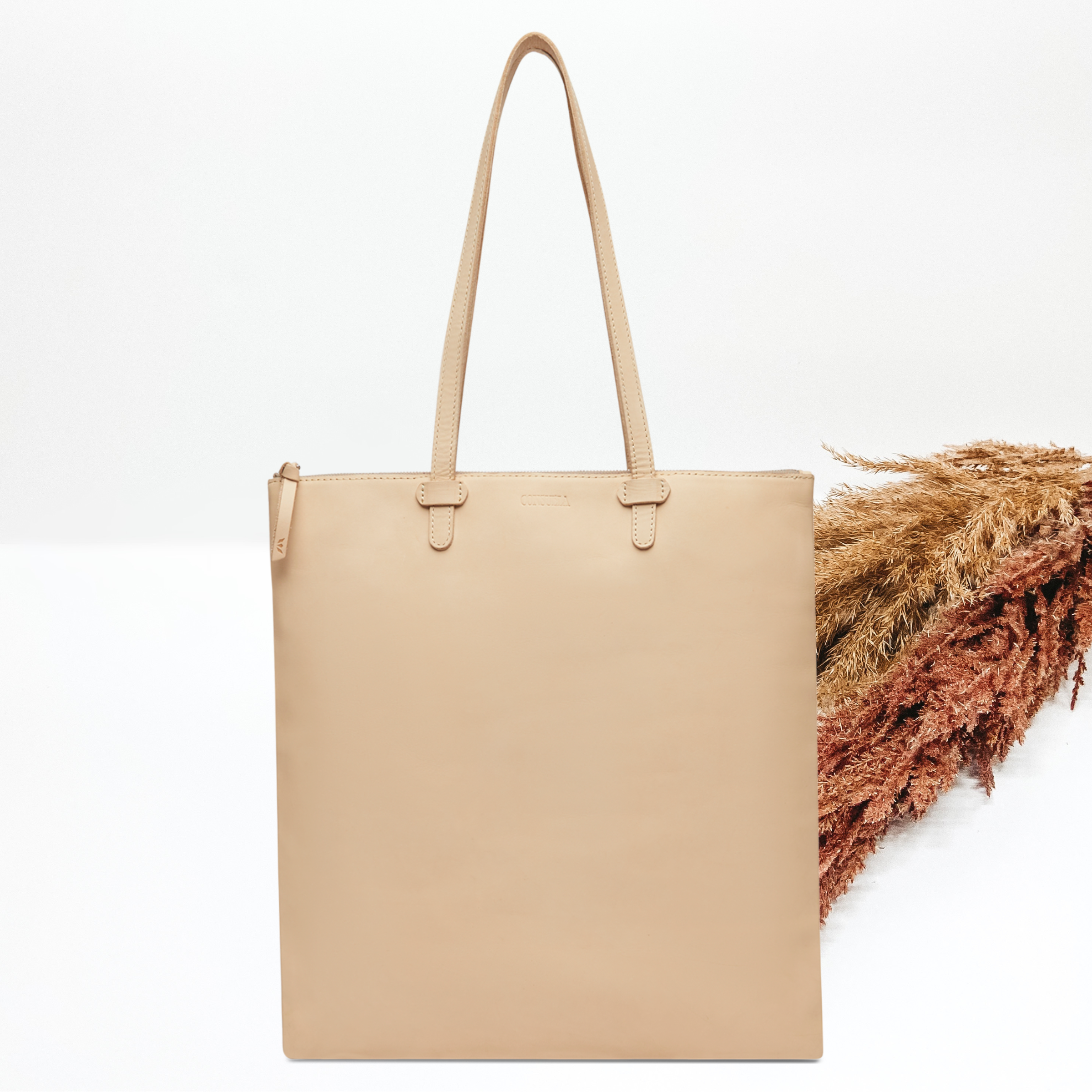Pictured on a white background is a light tan leather shopper tote with light tan handles. 
