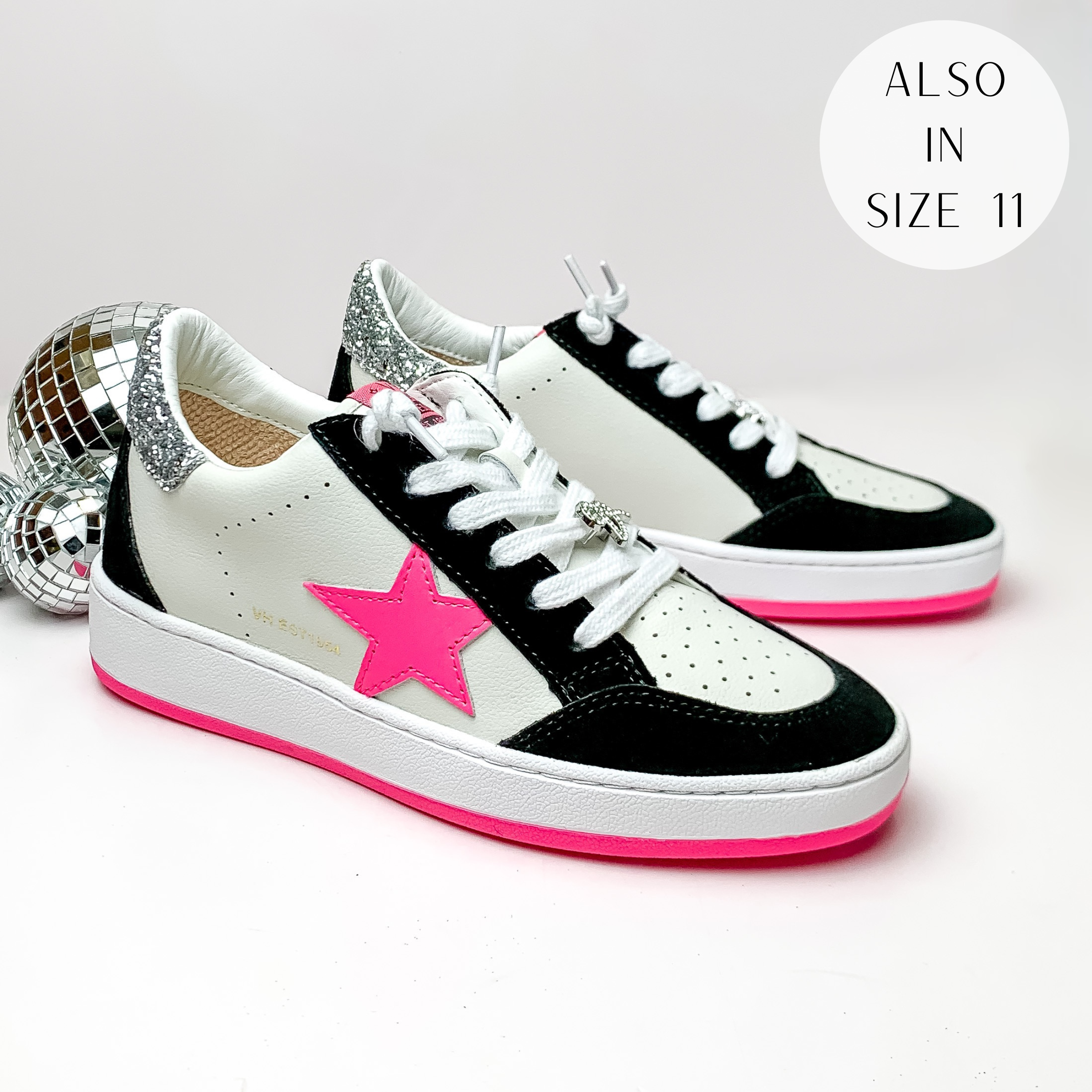 Pictured is a pair of white tennis shoes with black, silver glitter, and hot pik detailing. These shoes include a sliver glitter heel, a hot pink star on the side, and white laces. These shoes are pictured on a white background with disco balls on the left side