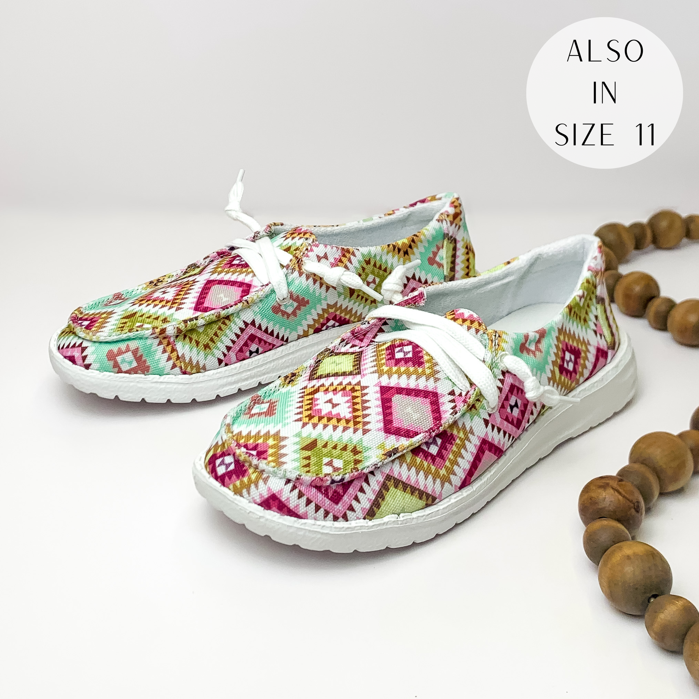 White shoes with a pink, red, green, teal, and yellow aztec print and white laces. These shoes are pictured on a white background with brown beads on the right side.