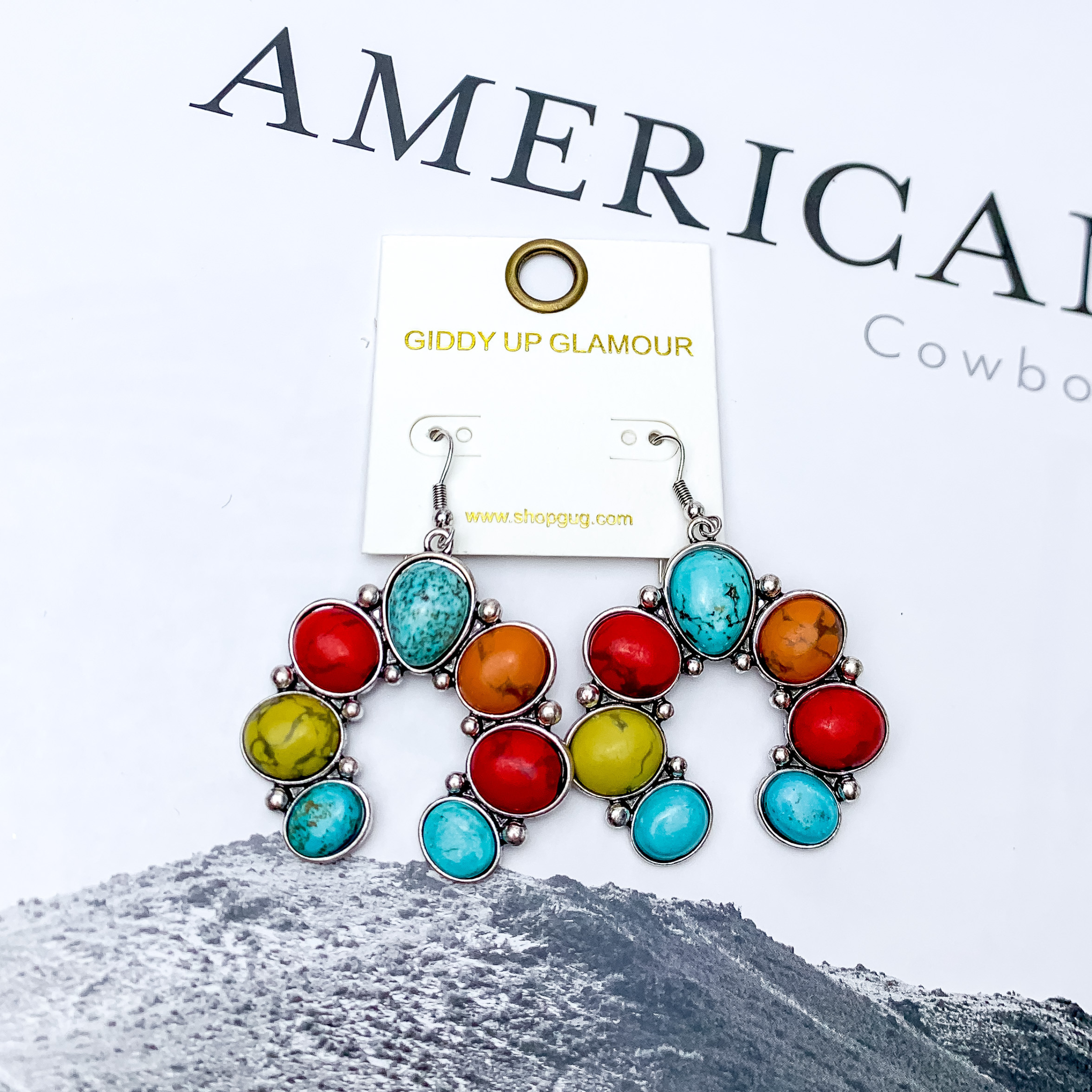Squash Blossom Stone Earrings In Multicolor. Pictured on a white background with a western scene in the back.