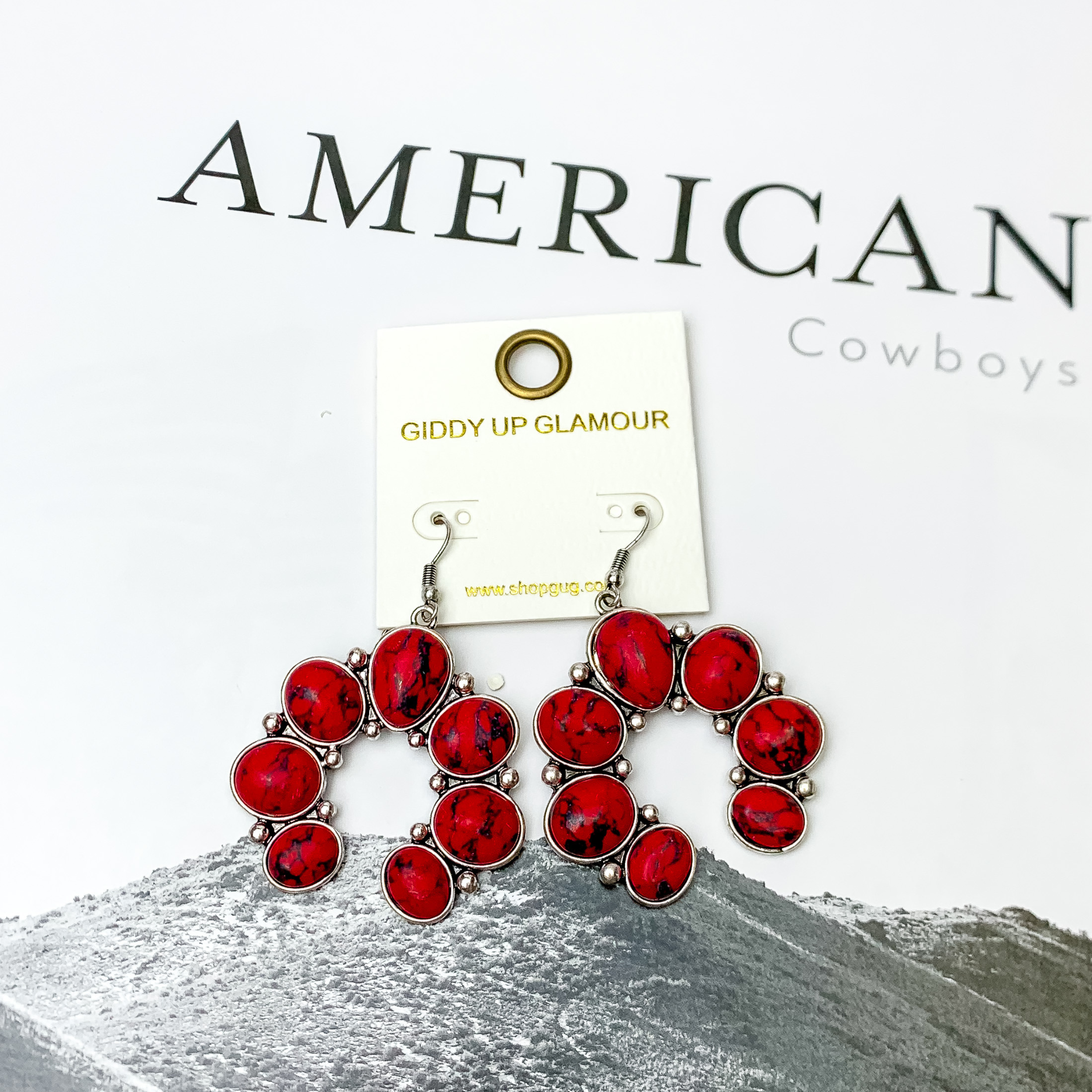 Squash Blossom Stone Earrings In Red. Pictured on a white background with a western scene in the back.