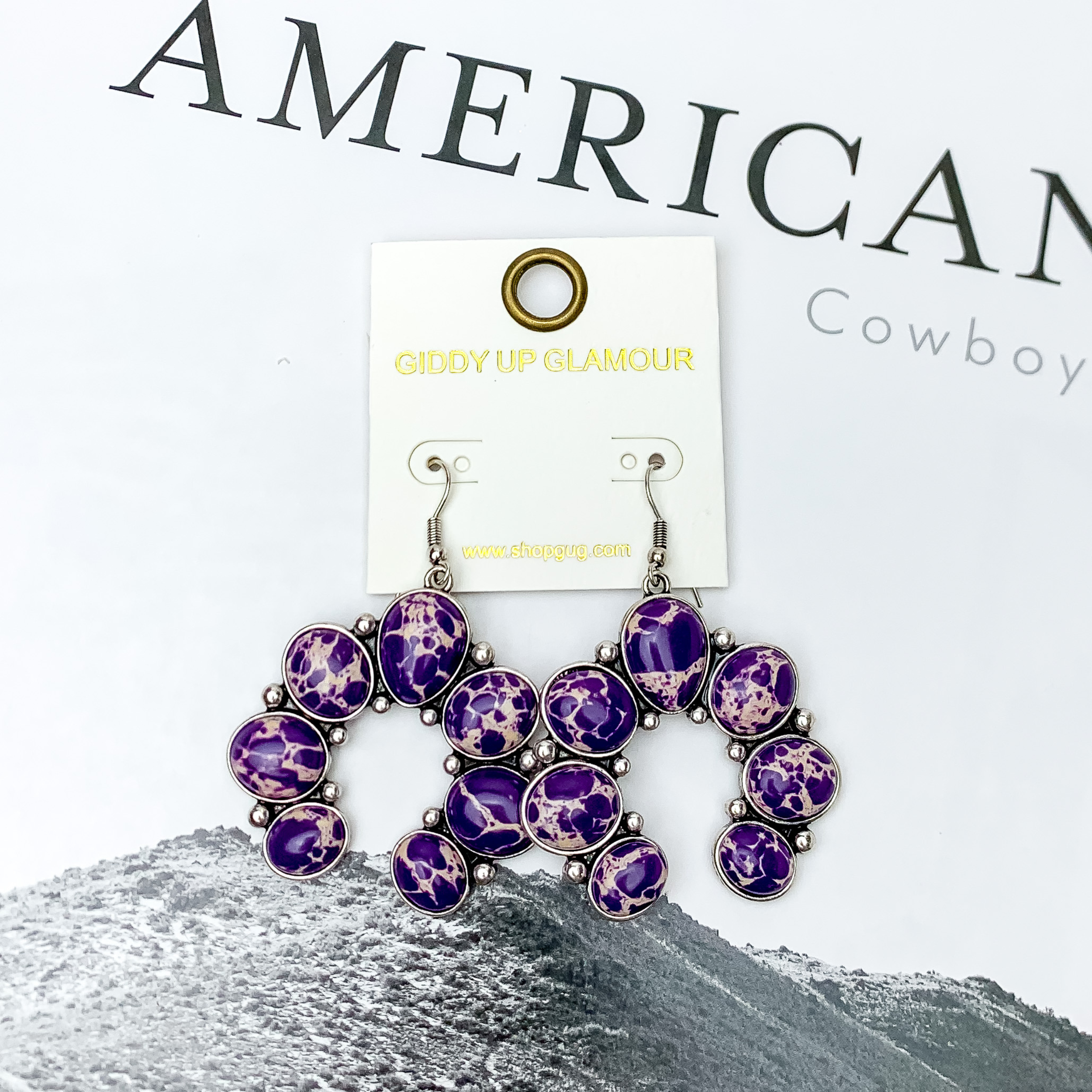 Squash Blossom Stone Earrings In Purple. Pictured on a white background with a western scene in the back.