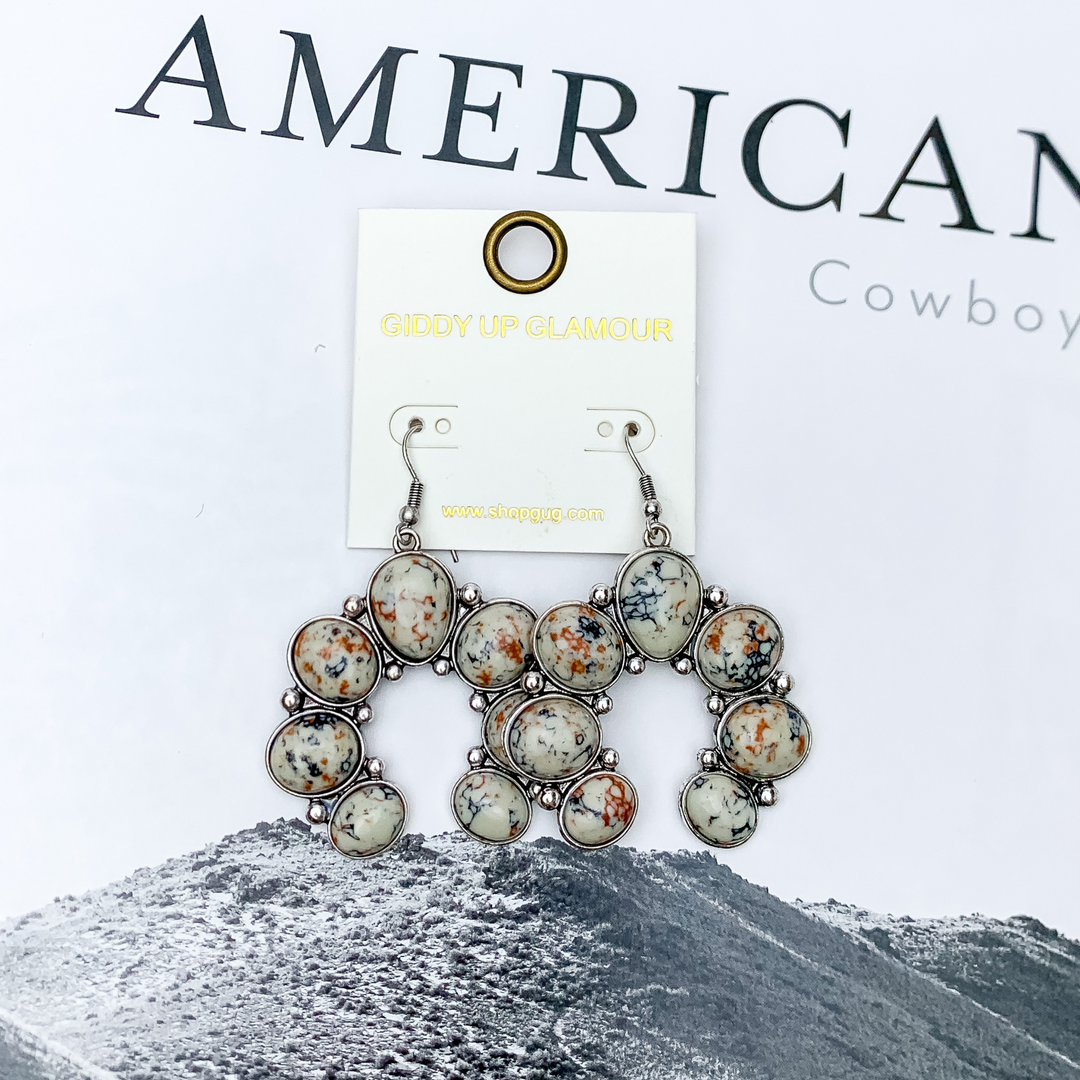 Squash Blossom Stone Earrings In Ivory Multicolor. Pictured on a white background with a western scene in the back.