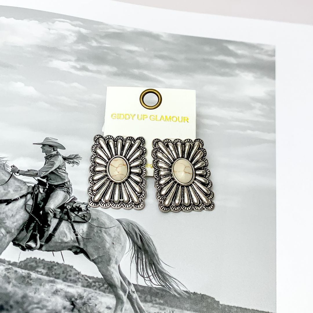 Western Flare Silver Tone Rectangle Earrings With Stone in White. Pictured on a western scene background.