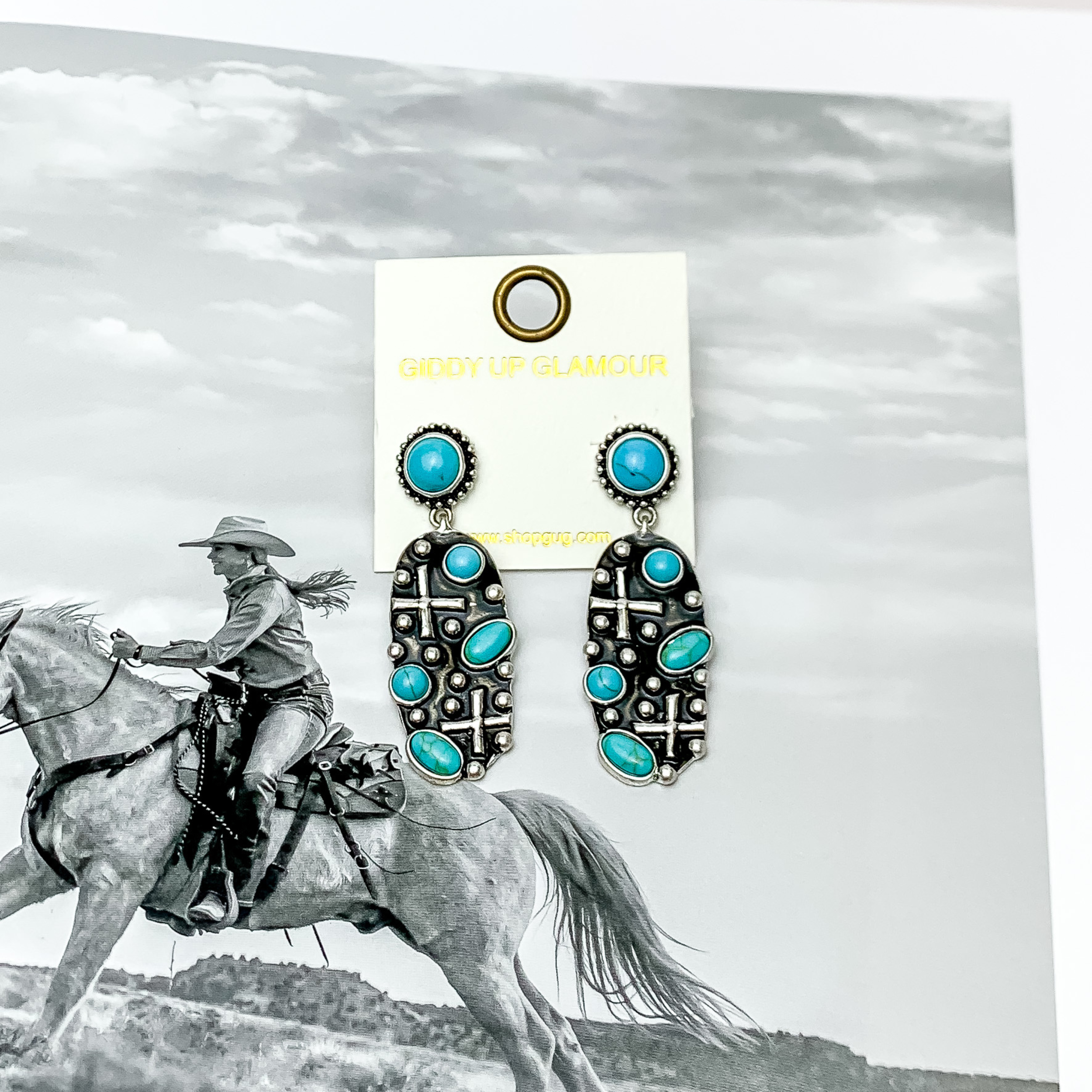 Western Silver Tone Designed Oval Earrings With Turquoise Stones. Pictured with a western scene in the background.