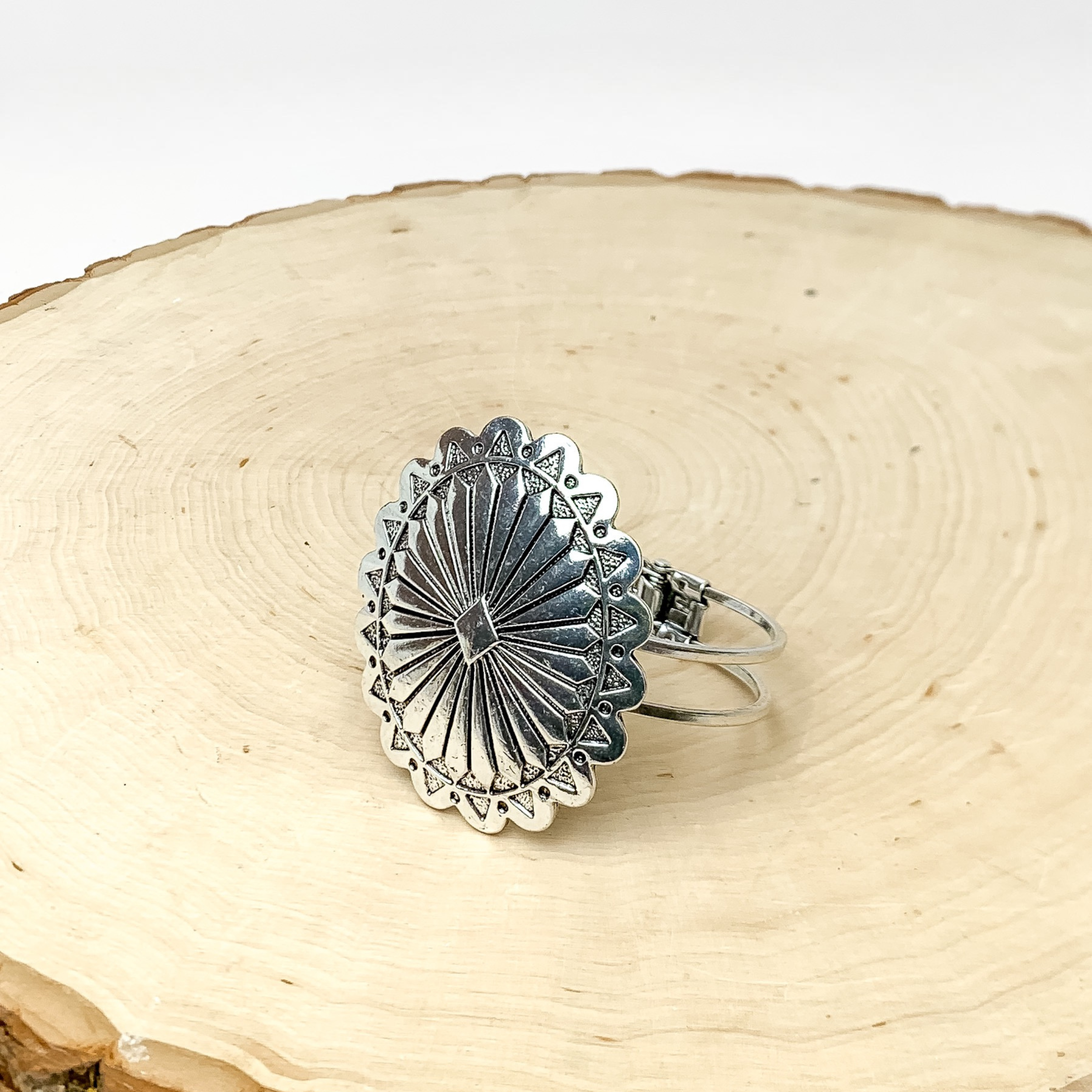 Western Oval Hinge Bracelet in Silver Tone With Turquoise Stone. Pictured sitting on a circular piece of wood. The background of the picture is white.