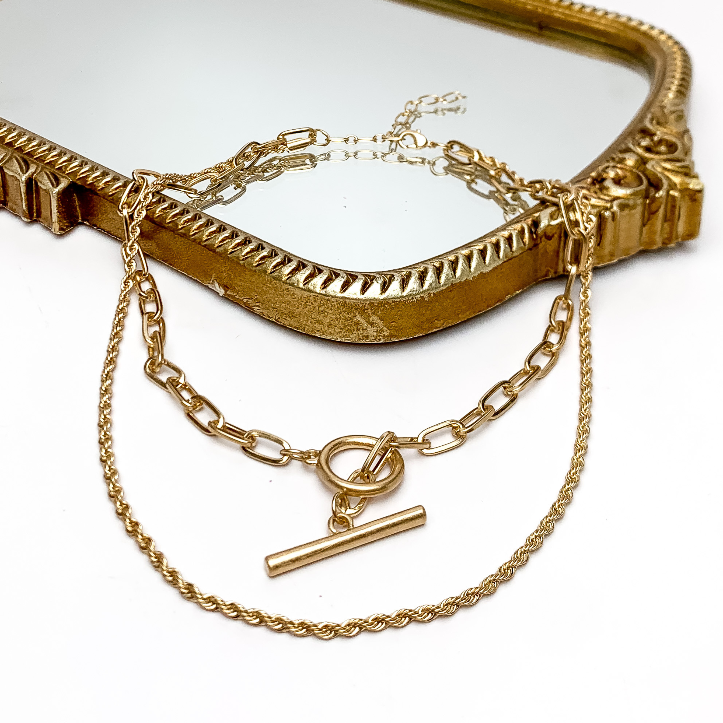 Tiki Gold Double Chain Necklace With Front Toggle. Pictured on a white background with part of the necklace laying on a gold trimmed mirror.