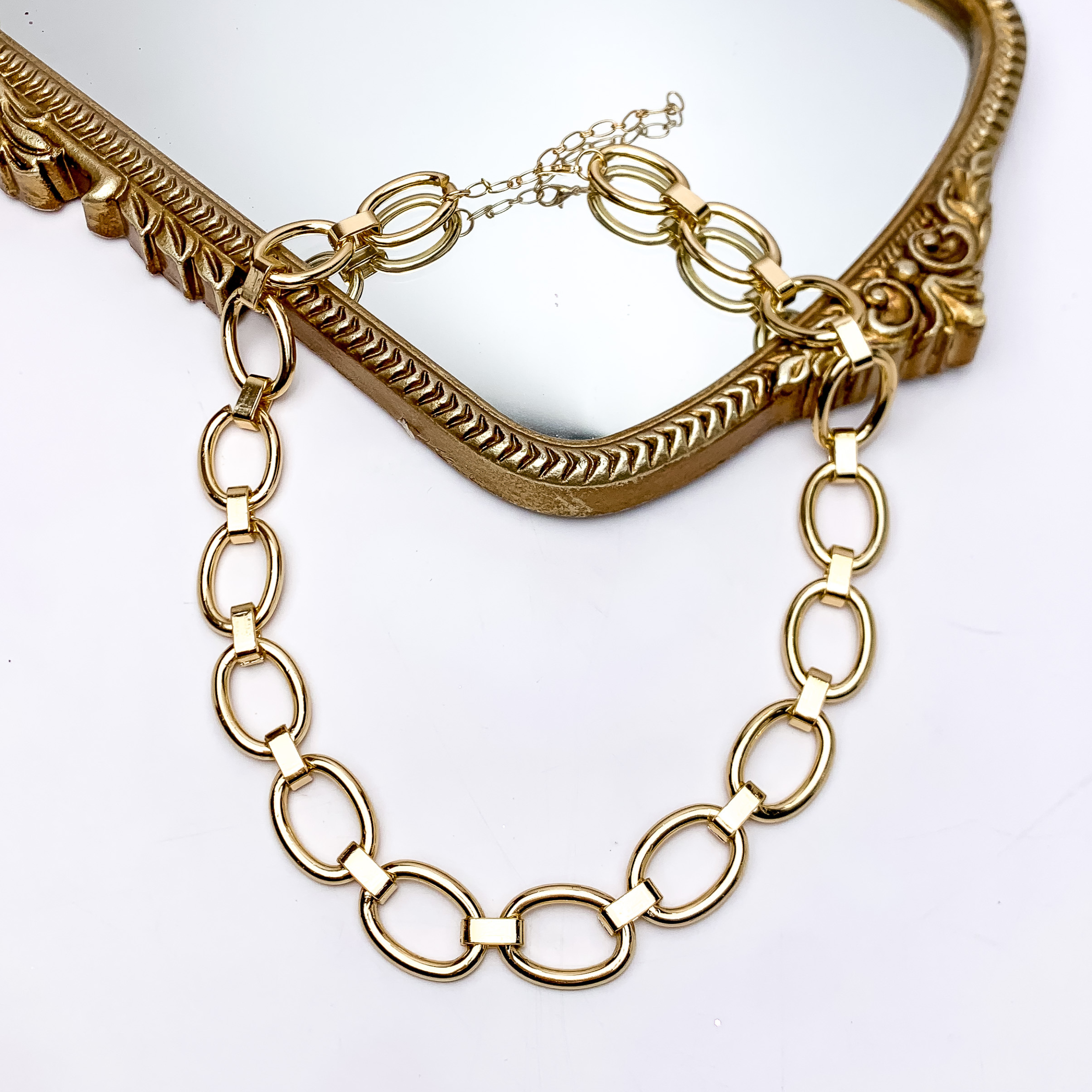Gold Tone Chain Necklace With Spacers. Pictured on a white background with part of the necklace on a gold framed mirror.