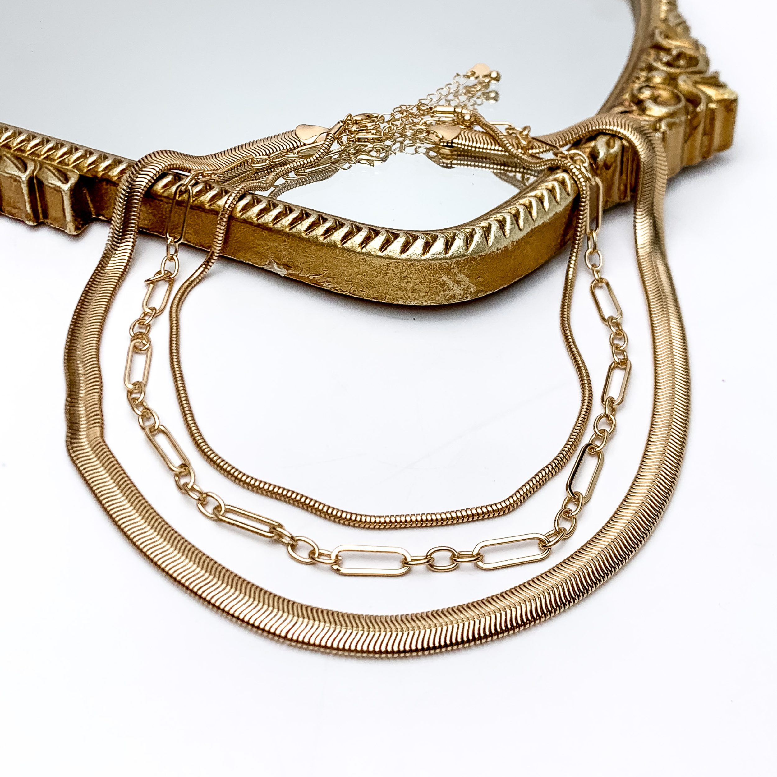 Island Metals Gold Tone Triple Strand Necklace. Pictured on a white background with part of the necklace on a gold framed mirror.
