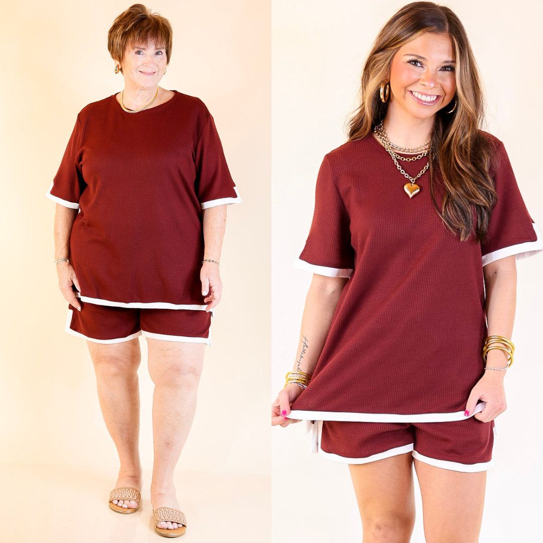 Two women wearing matching maroon outfits with white trim on a beige background