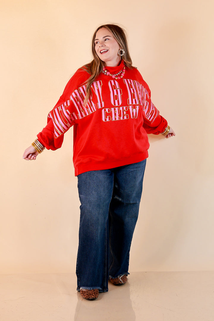 Merry Company red oversized mock neck sweatshirt with pink and red striped Merry and Bright Crew lettering outlined in gold, styled with dark wash jeans