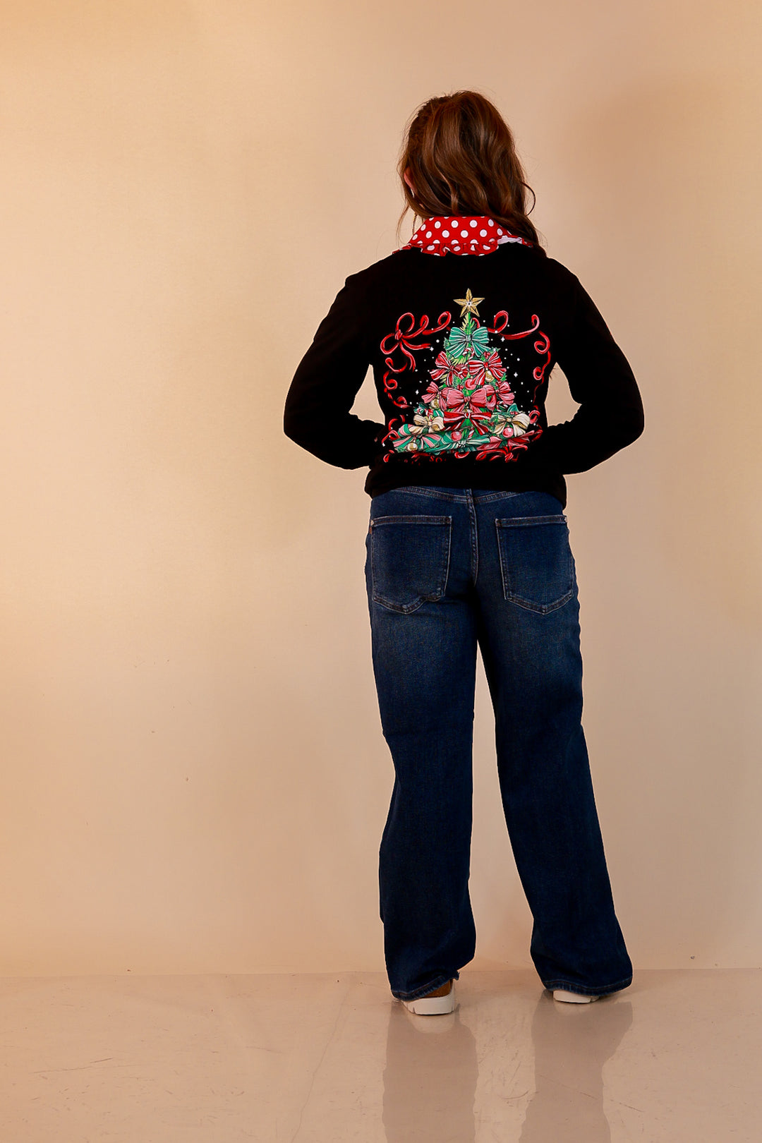 Trimmed to Perfection black long sleeve graphic tee back view with bow Christmas tree graphic, styled with a red polka dot collar and dark wash jeans