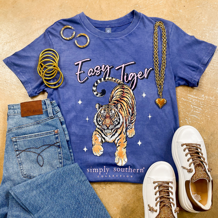 Blue t-shirt with tiger graphic and 'Easy Tiger' text, paired with jeans and sneakers on a beige background.