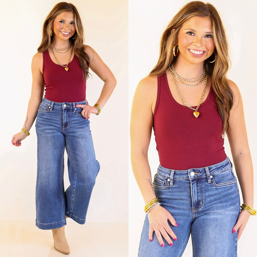 model wearing a maroon bodysuit and blue jeans on a plain background