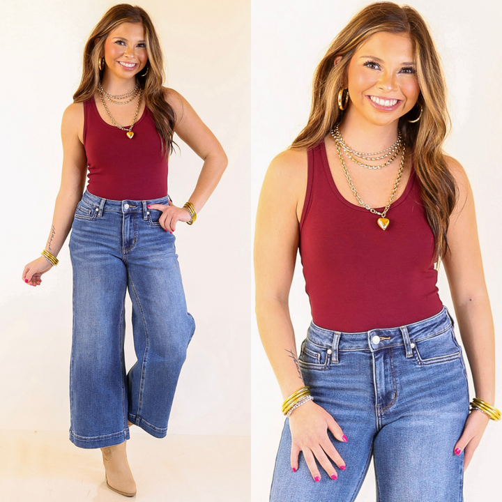 model wearing a maroon bodysuit and blue jeans on a plain background