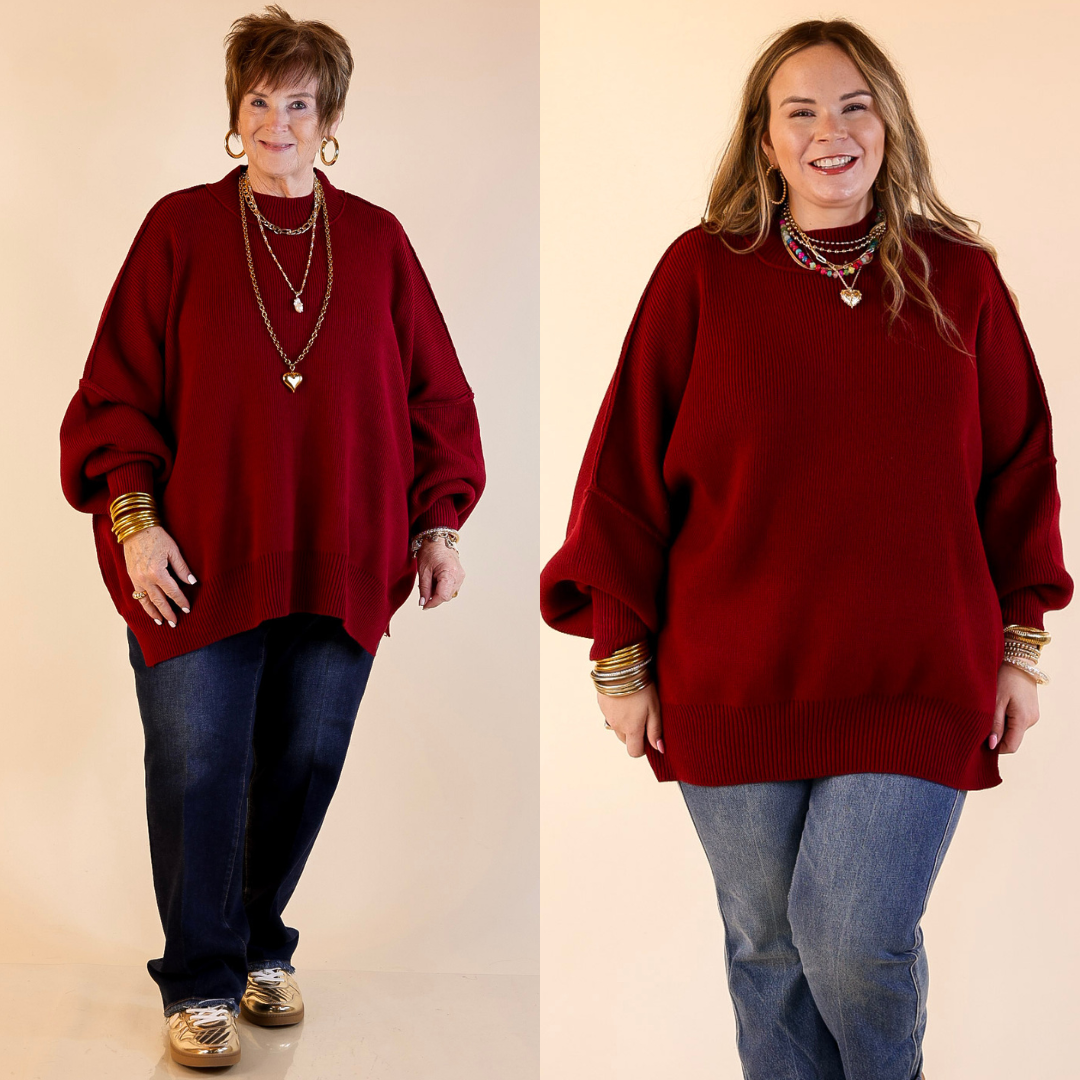 Models are wearing maroon oversized sweater with side slit. One model is showcasing a smaller size while the other is wearing a larger size, with jeans.