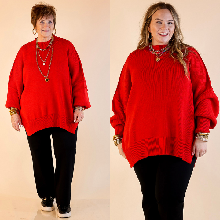 Models are wearing red oversized sweater with side slit. One model is showcasing a smaller size while the other is wearing a larger size, both in combination with black pants and flat shoes.