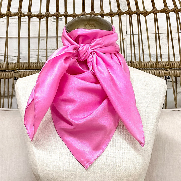 Mannequin head with a pink scarf draped over its neck, sitting on a wicker chair.