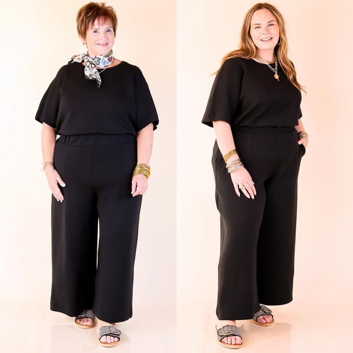 Two women wearing matching black outfits against a plain background