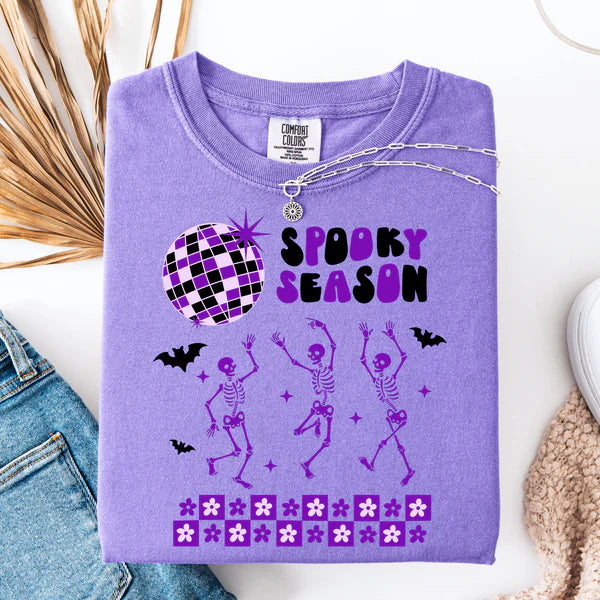 Purple t-shirt with Halloween-themed design featuring skeletons and a disco ball on a white surface.