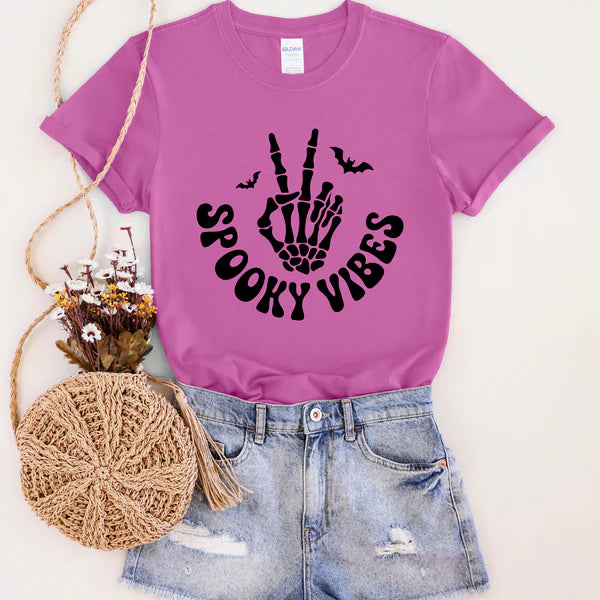 Purple t-shirt with 'Spooky Vibes' design, paired with denim shorts and a round woven bag on a light background.