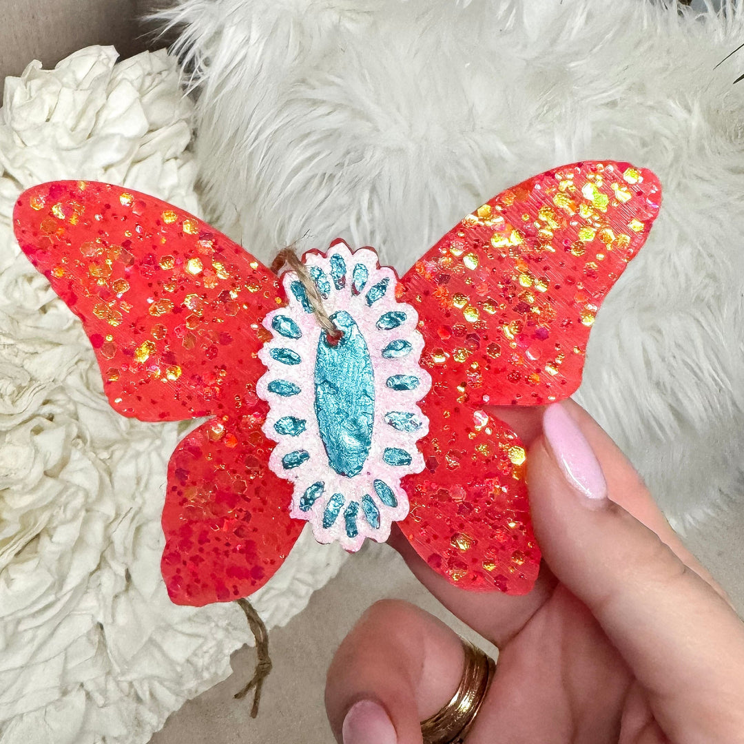 Hand holding a red butterfly-shaped object with decorative elements against a neutral background