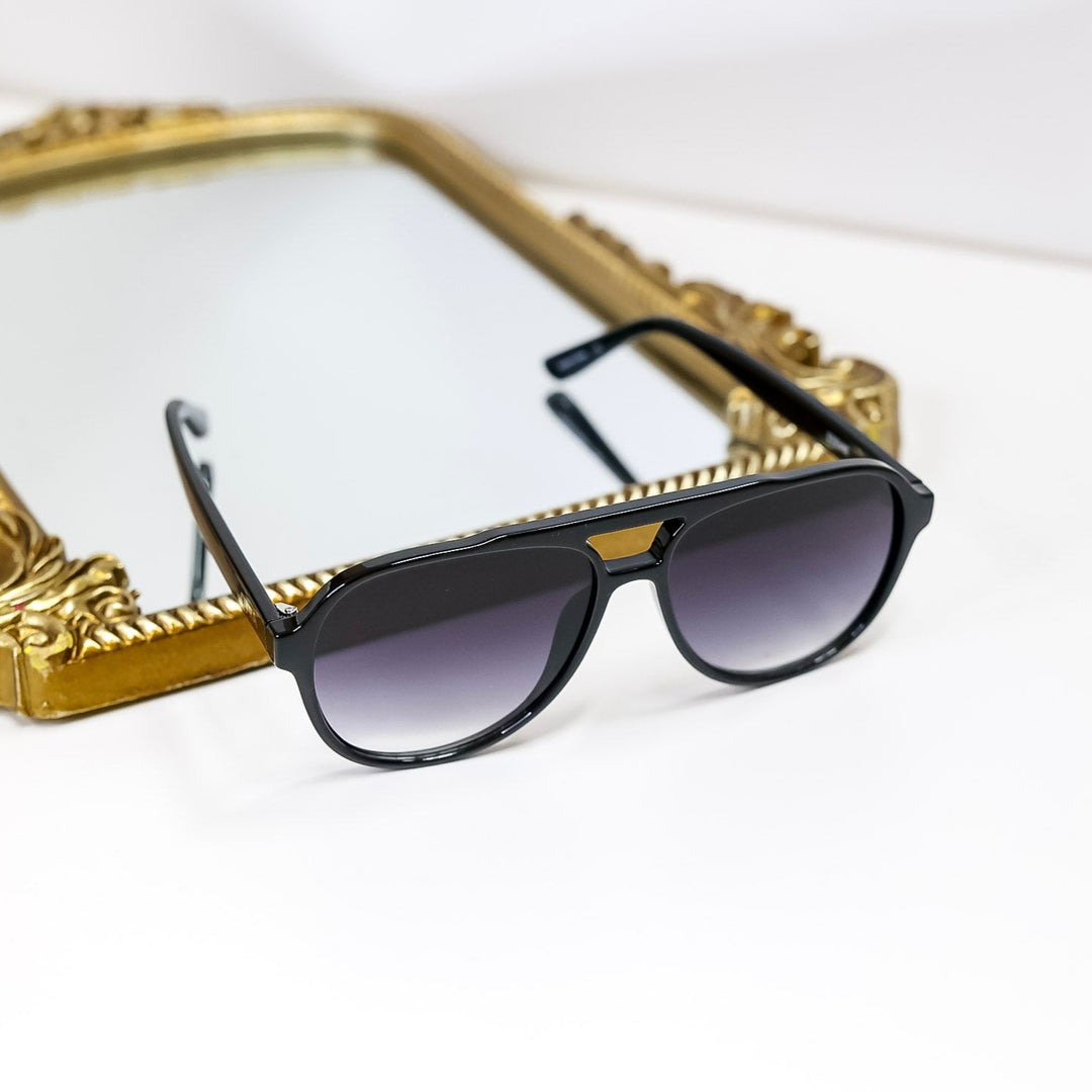 Black sunglasses on a white surface with a gold decorative frame in the background
