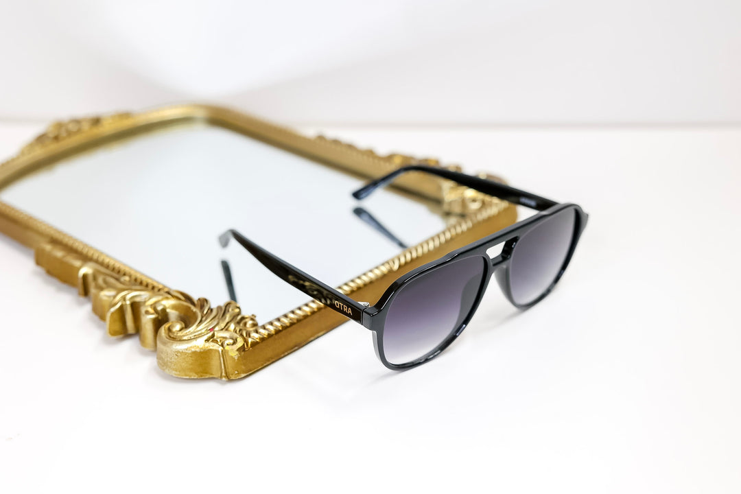 Black sunglasses on a white surface with a decorative gold frame in the background
